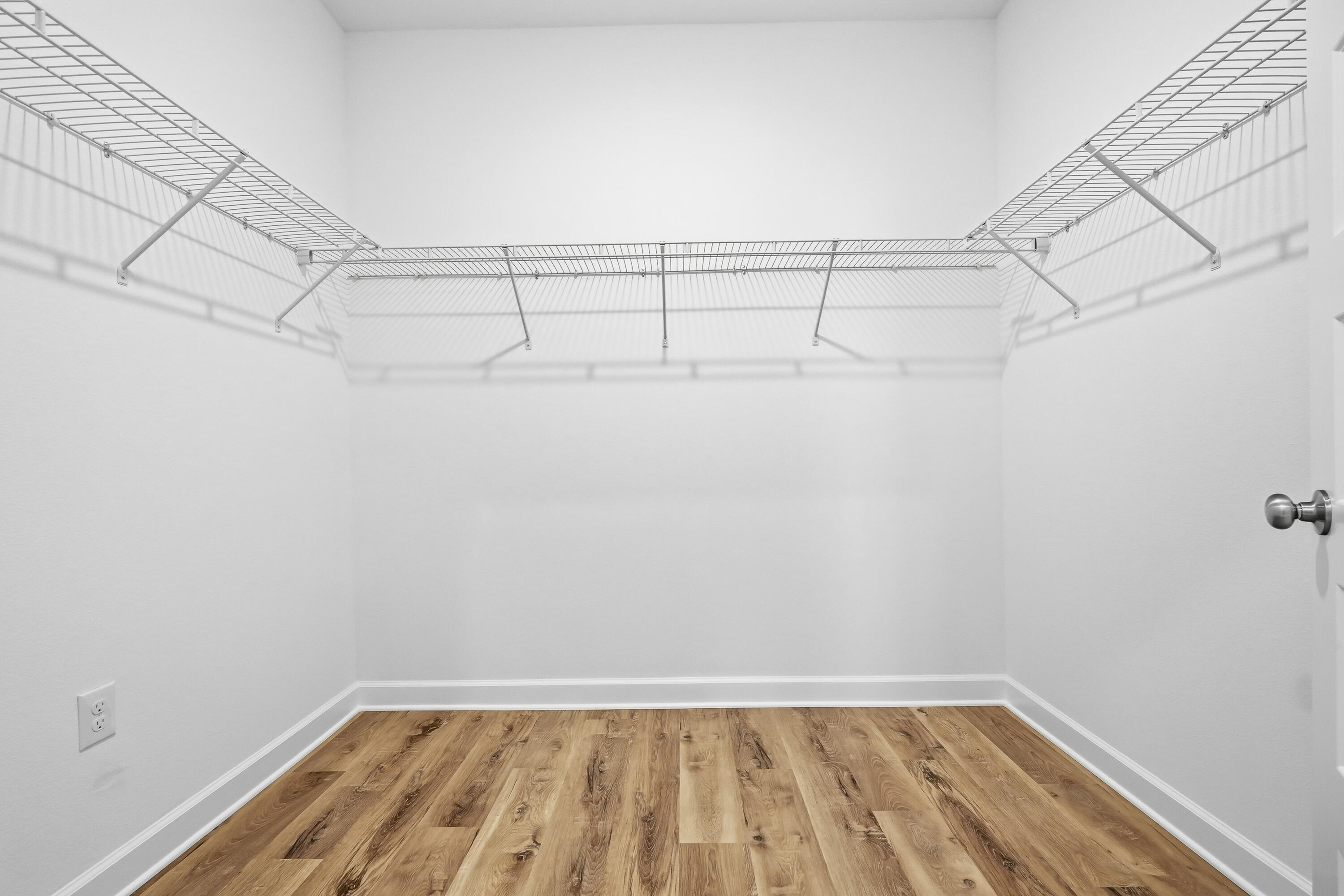 Empty walk-in closet with wraparound wire shelving and wood-look flooring.