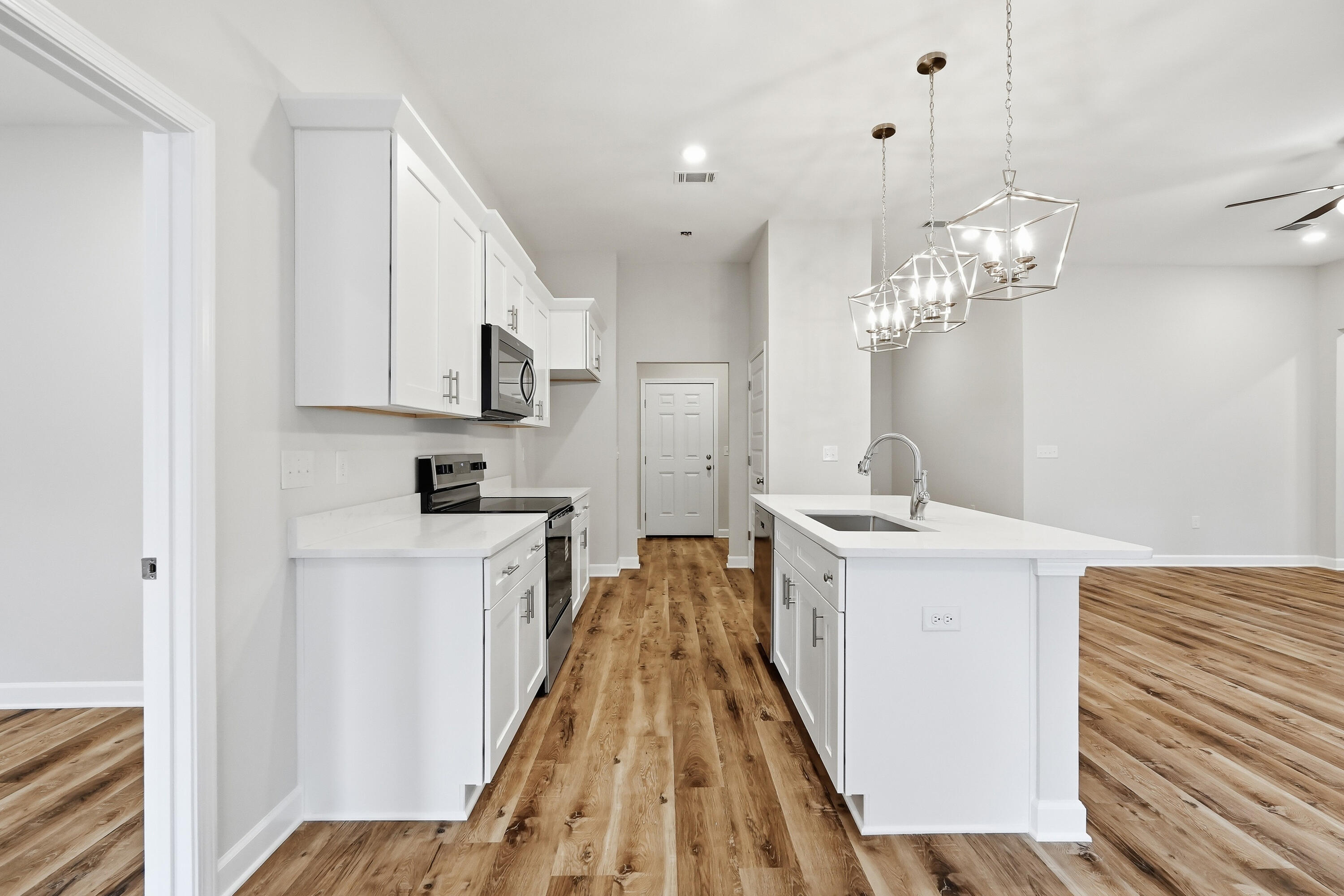 Kitchen with white cabinets, a large island, geometric pendant lights, and wood-look flooring.