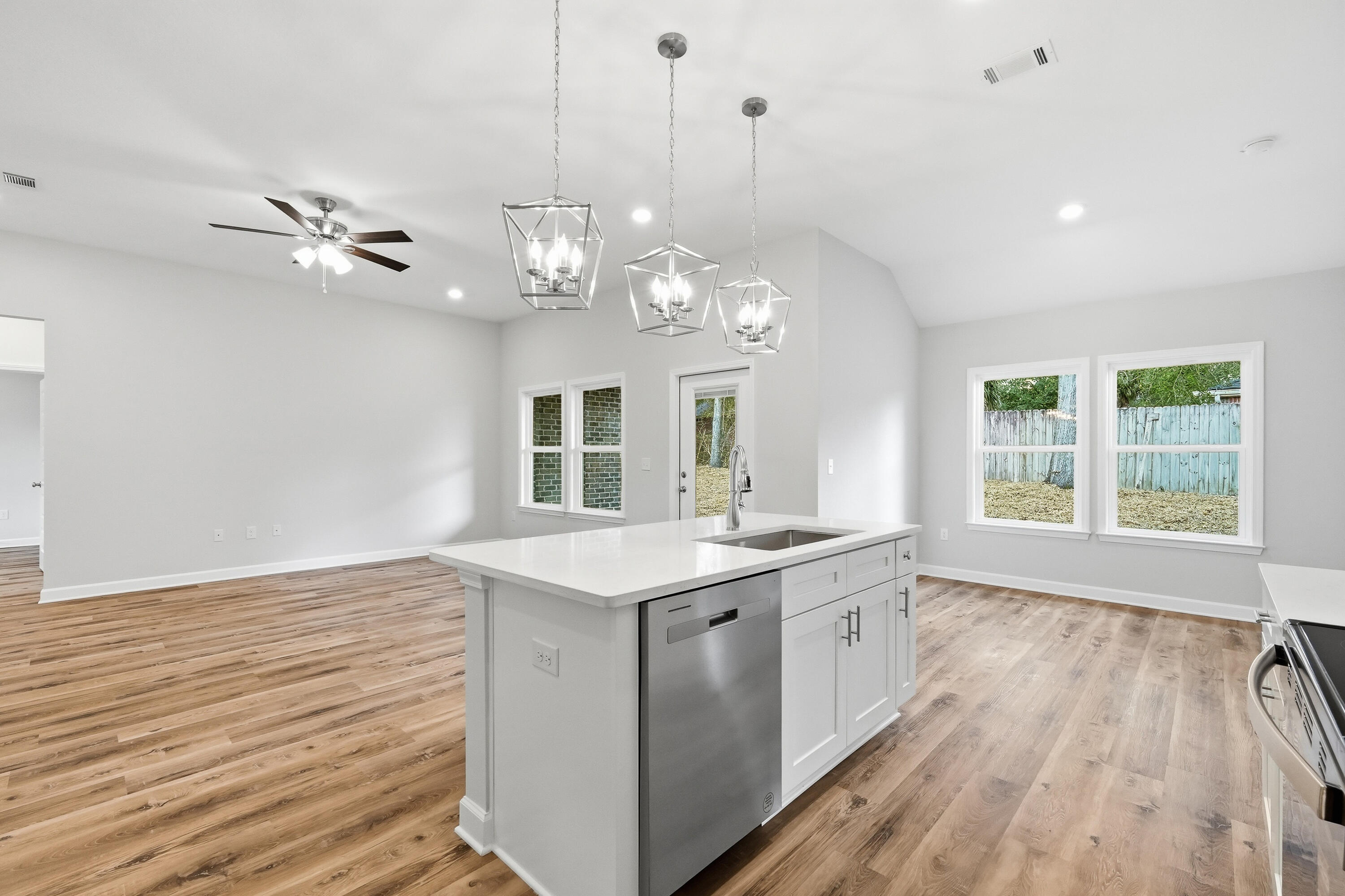 Open-plan kitchen with a large white island, stainless dishwasher, and three pendant lights.