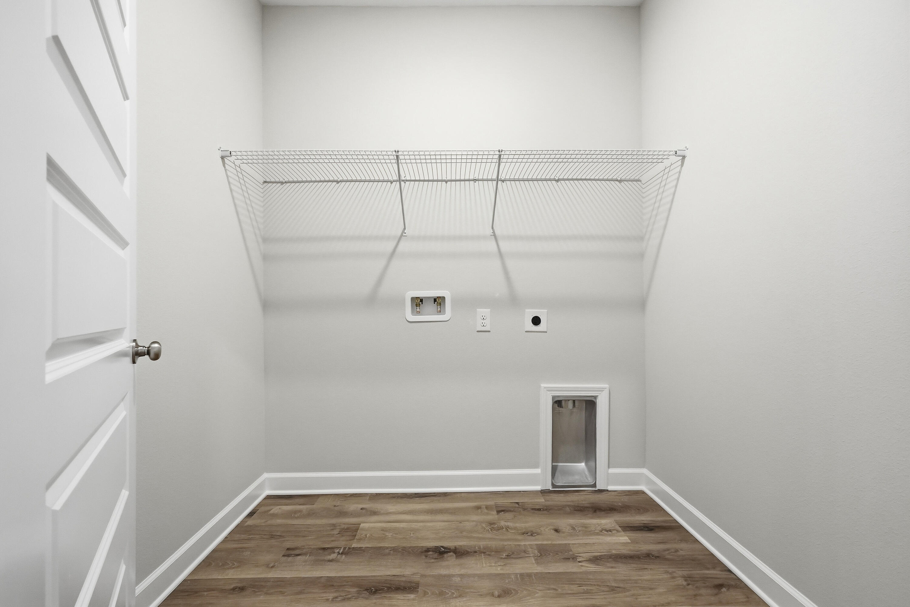 Empty laundry room with wire shelving, washer hookups, and a small pet door.