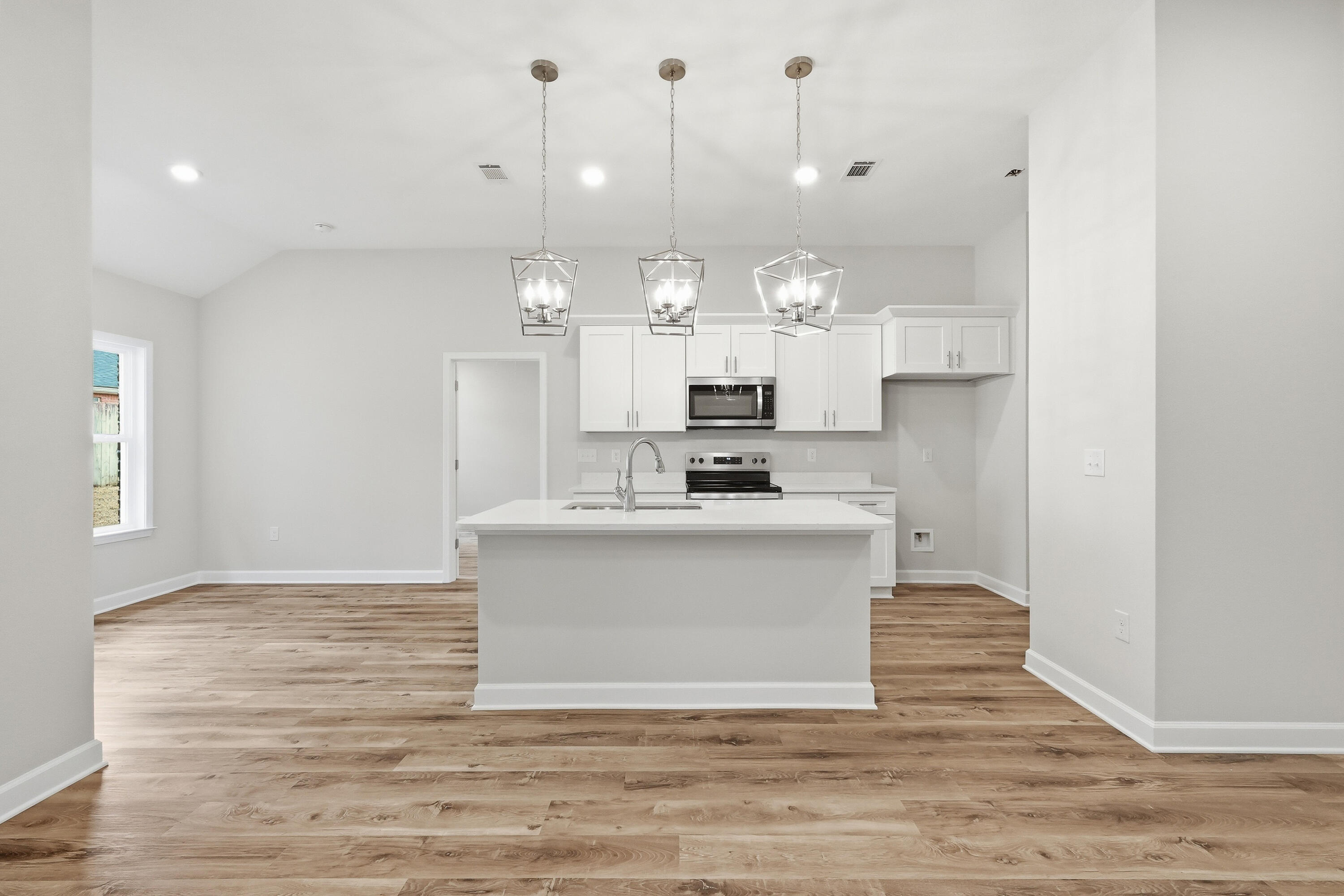 Vacant kitchen with a large white island, pendant lights, and wood-look plank flooring.