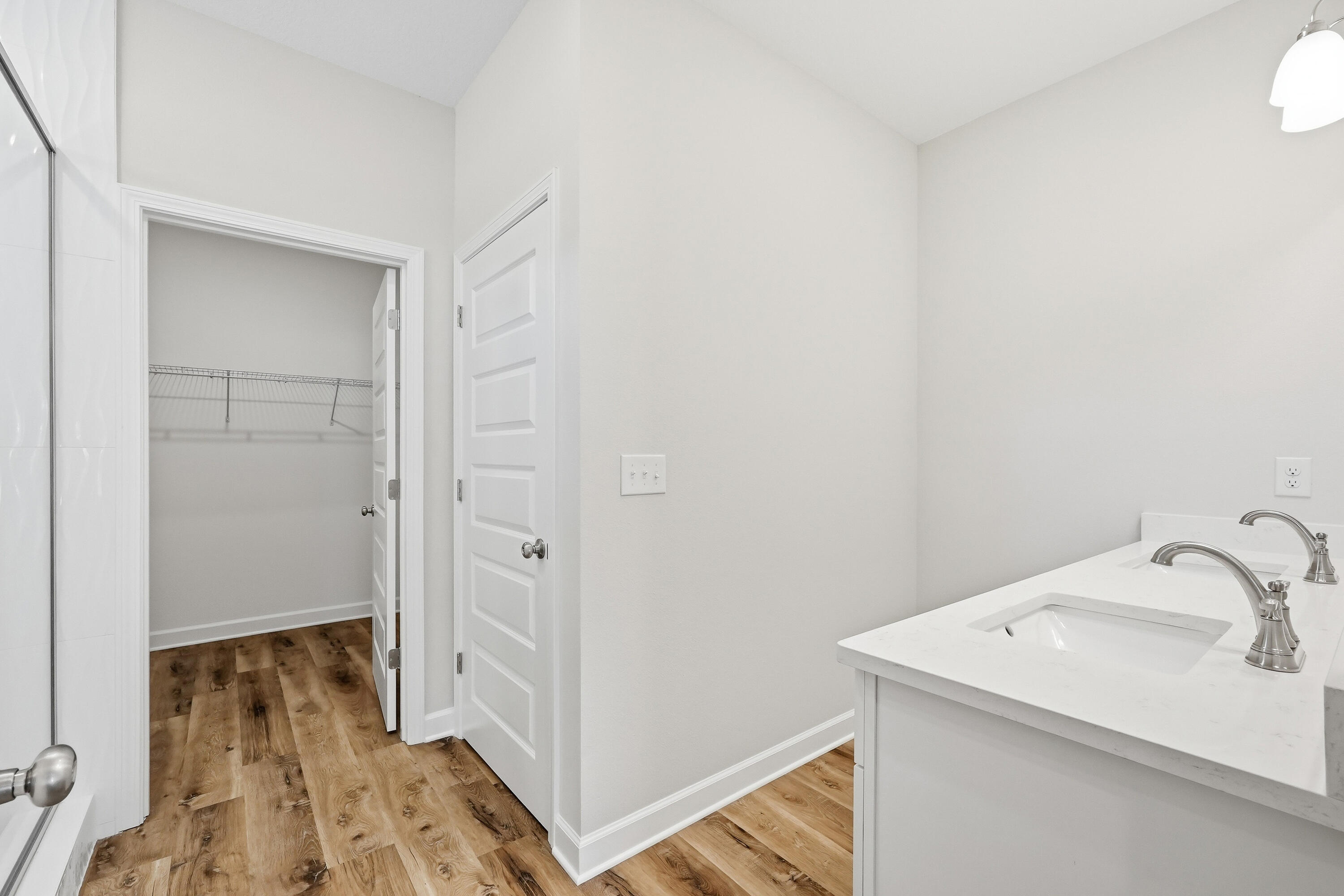 Bathroom with a double-sink vanity, wood-look floors, and an open walk-in closet.