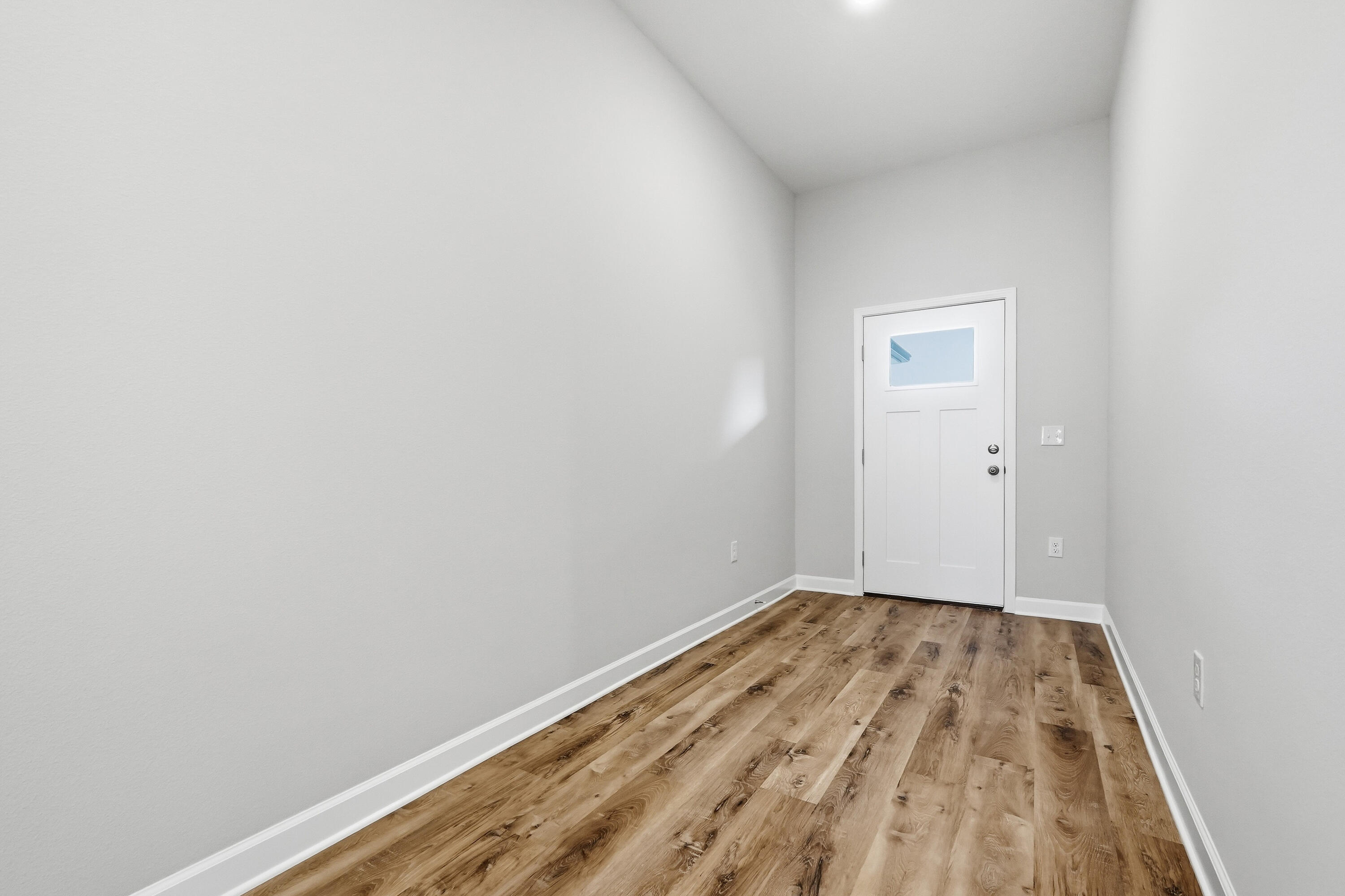 Empty entryway with wood-look plank flooring and a white front door.
