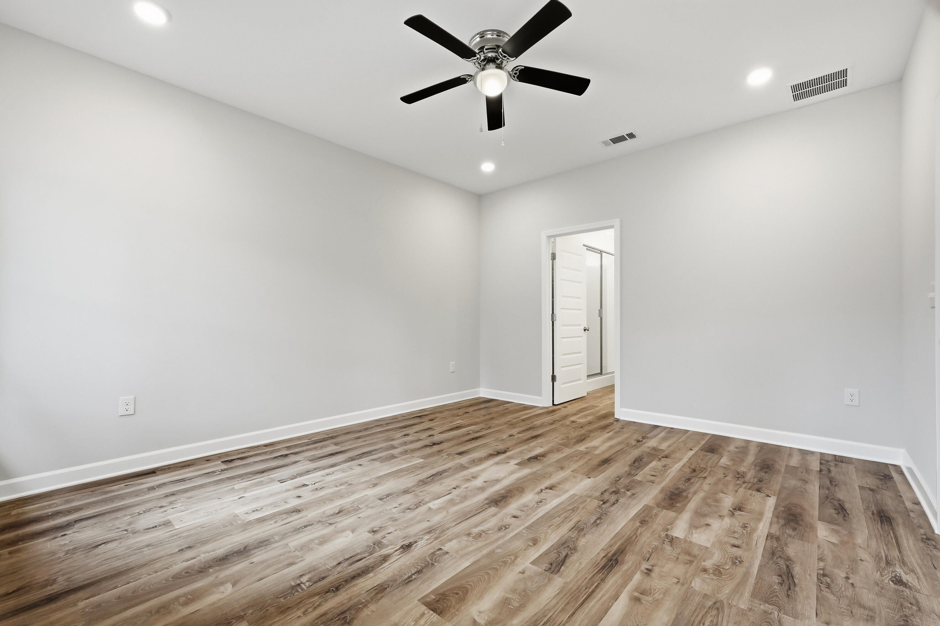 Empty bedroom with wood-look flooring, a black ceiling fan, and an open bathroom doorway.