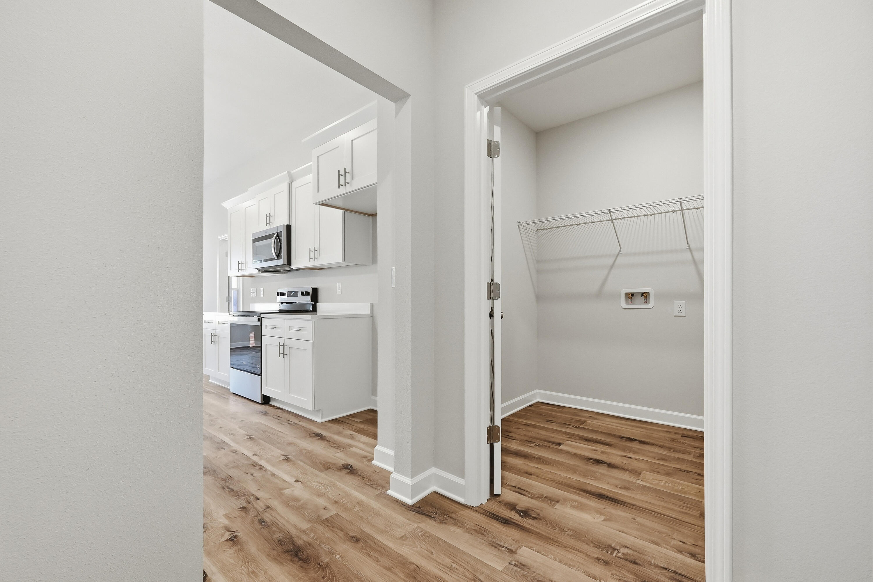 Laundry closet with wire shelf and hookups beside a white kitchen with stainless steel appliances.