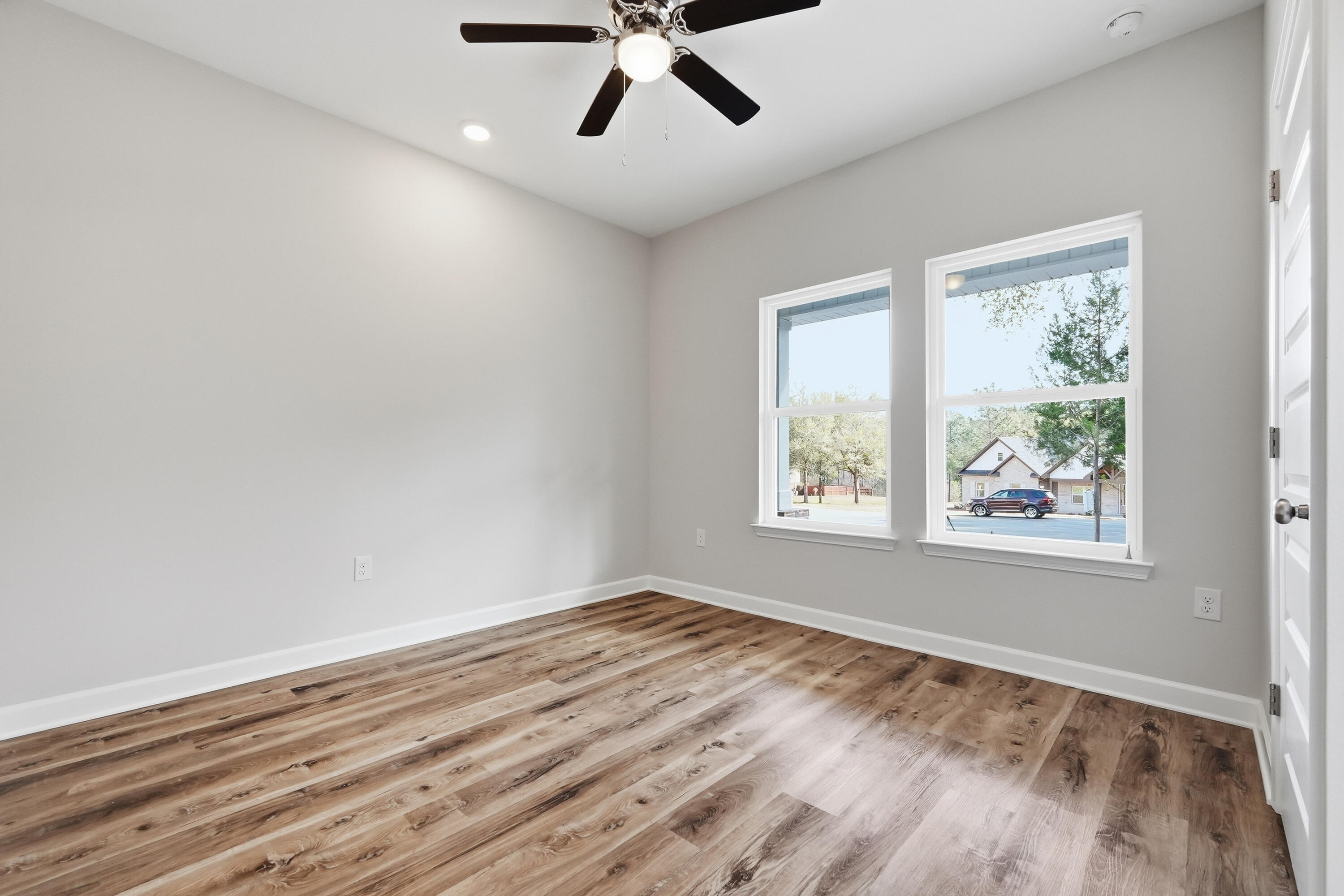 Empty bedroom with wood-look floors, two windows, and a dark ceiling fan.