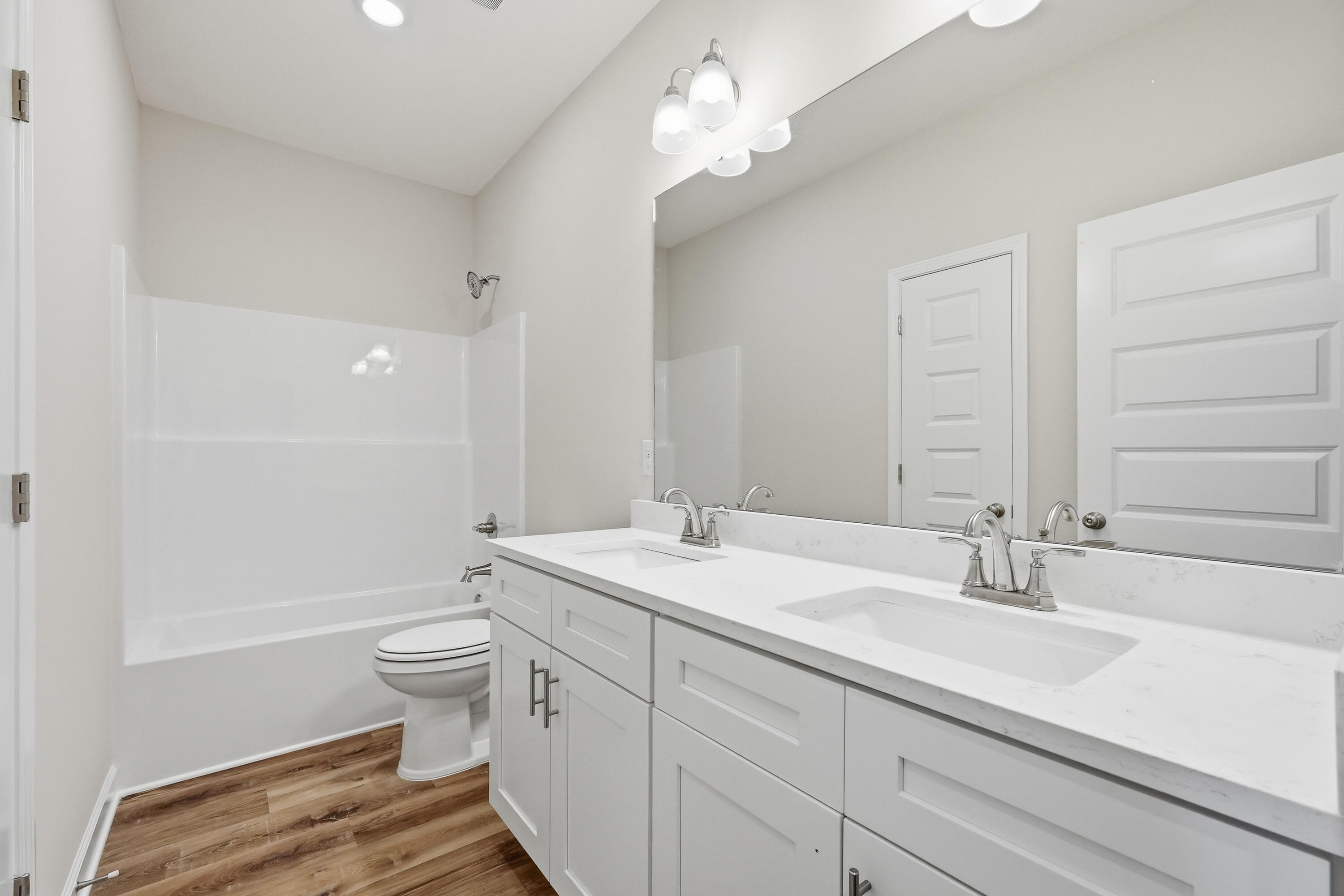 Bathroom with a white double vanity and tub-shower combination, finished with wood-look flooring.