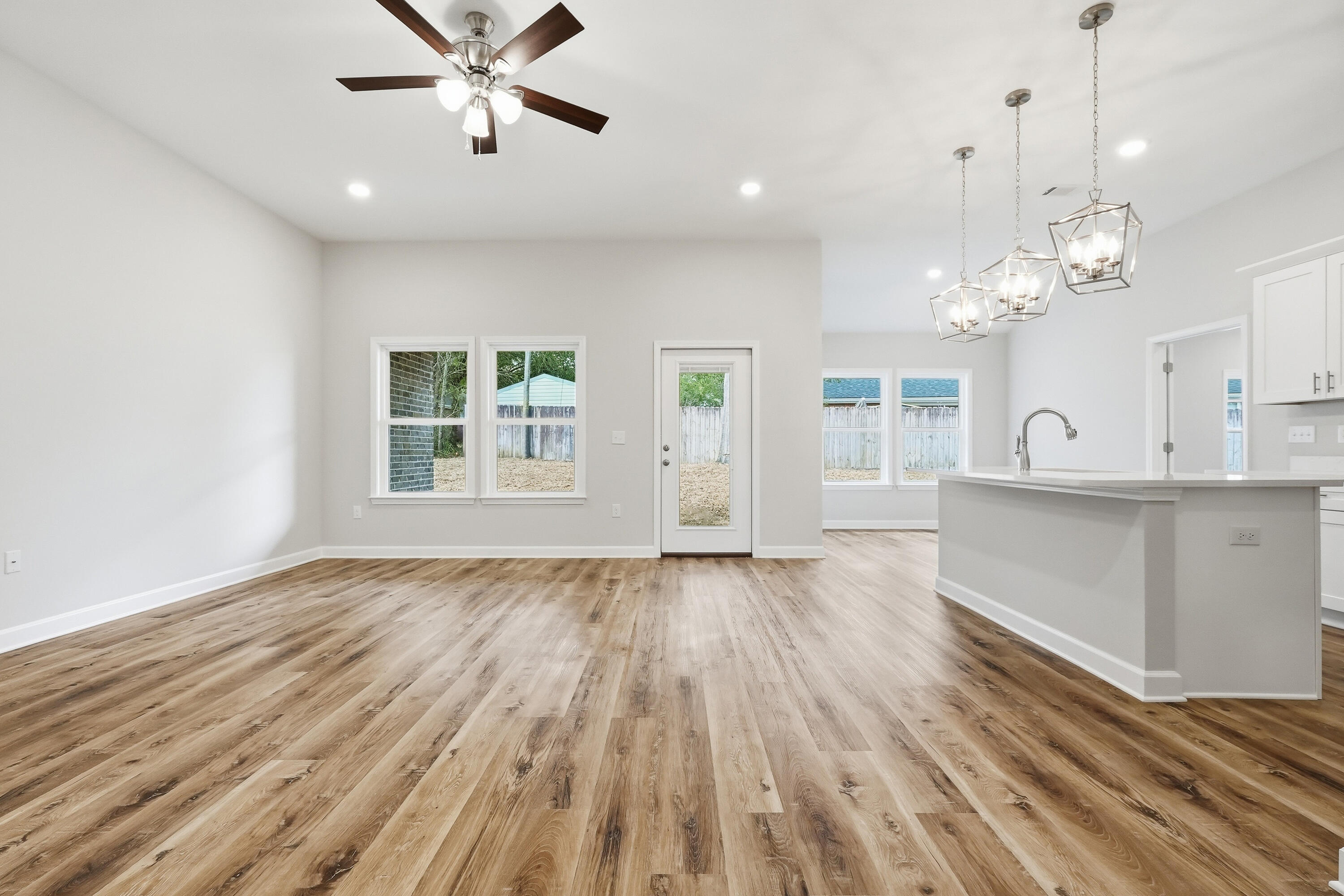 Open kitchen and dining area with a white island, wood-look floors, and geometric pendant lights.