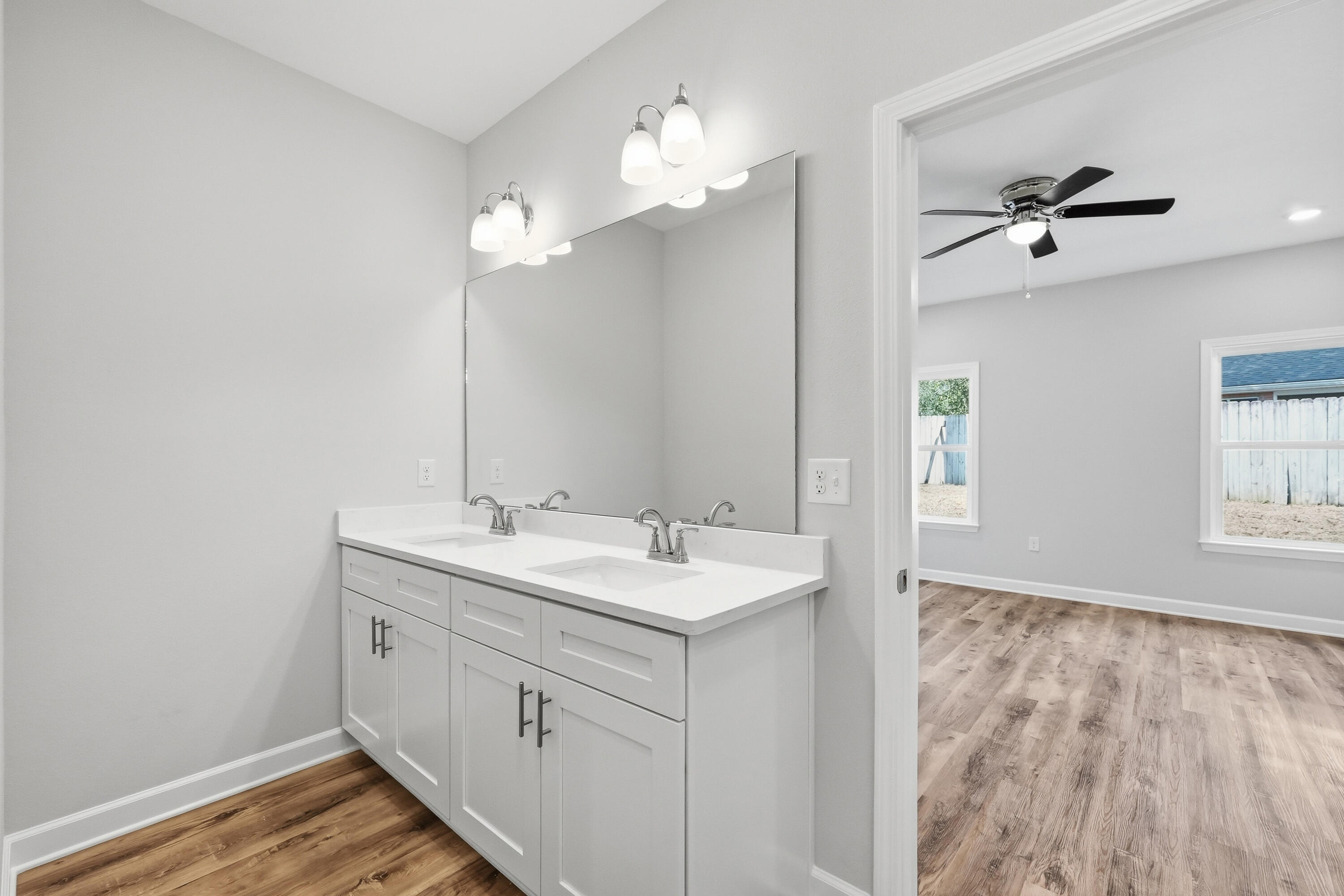 Bathroom with a double-sink vanity and large mirror, opening to an unfurnished bedroom.
