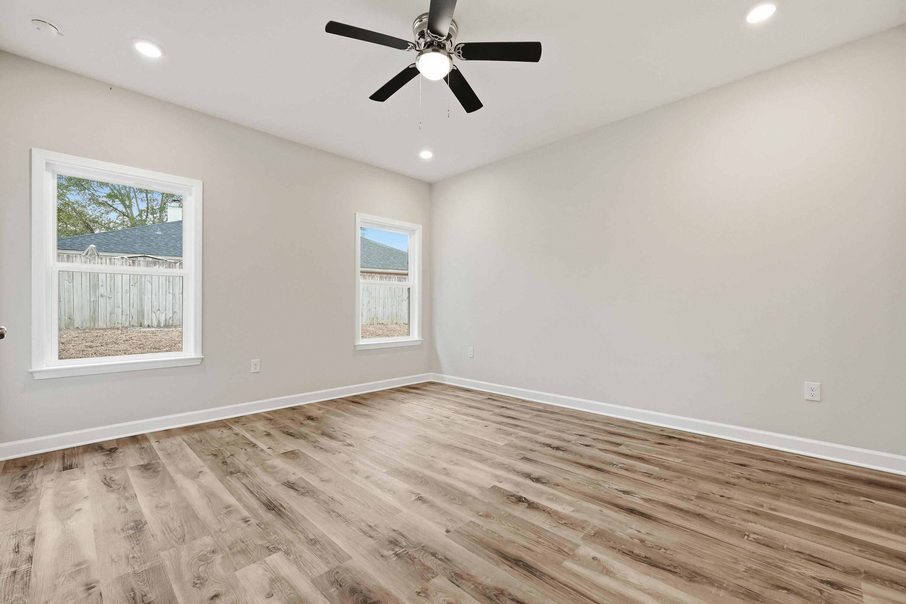 Empty bedroom with wood-look flooring, two windows, and a black ceiling fan.