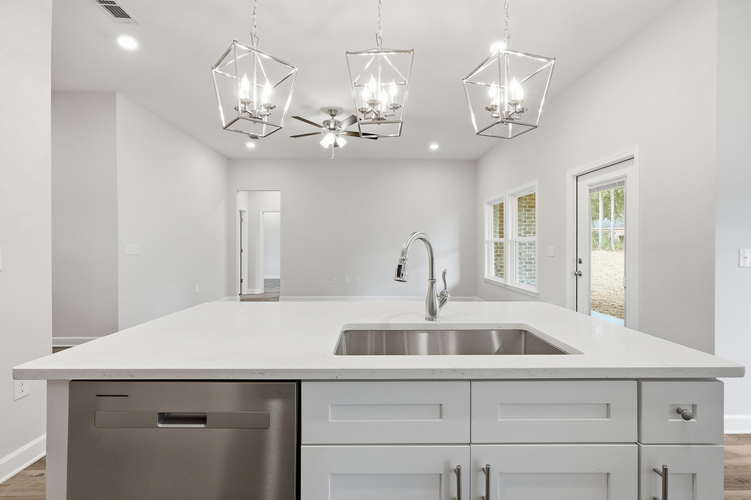 Vacant kitchen with a large white island, stainless sink, and three geometric pendant lights.