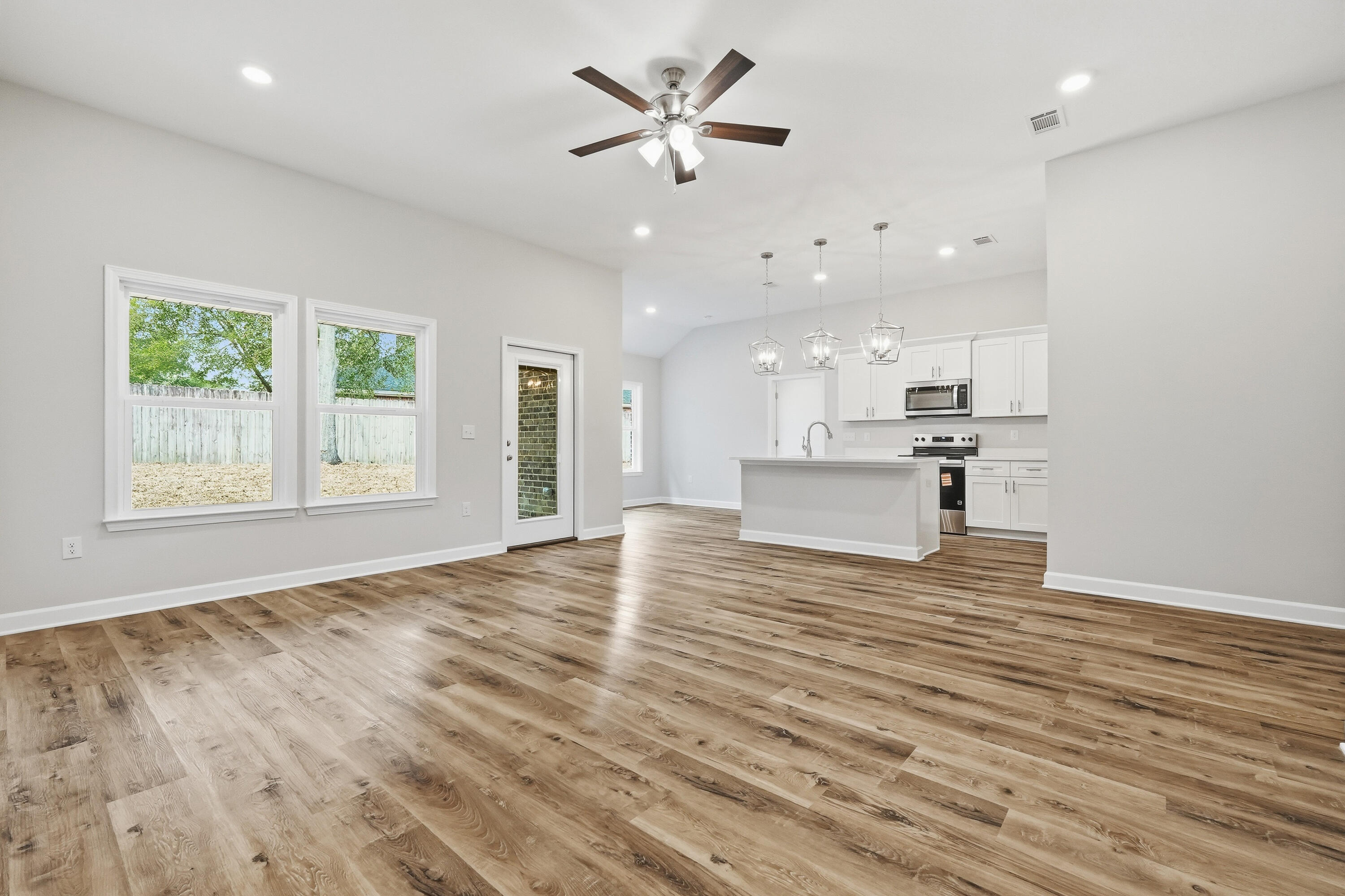 Open-plan living area and kitchen with wood-look floors, white cabinets, and a central island.