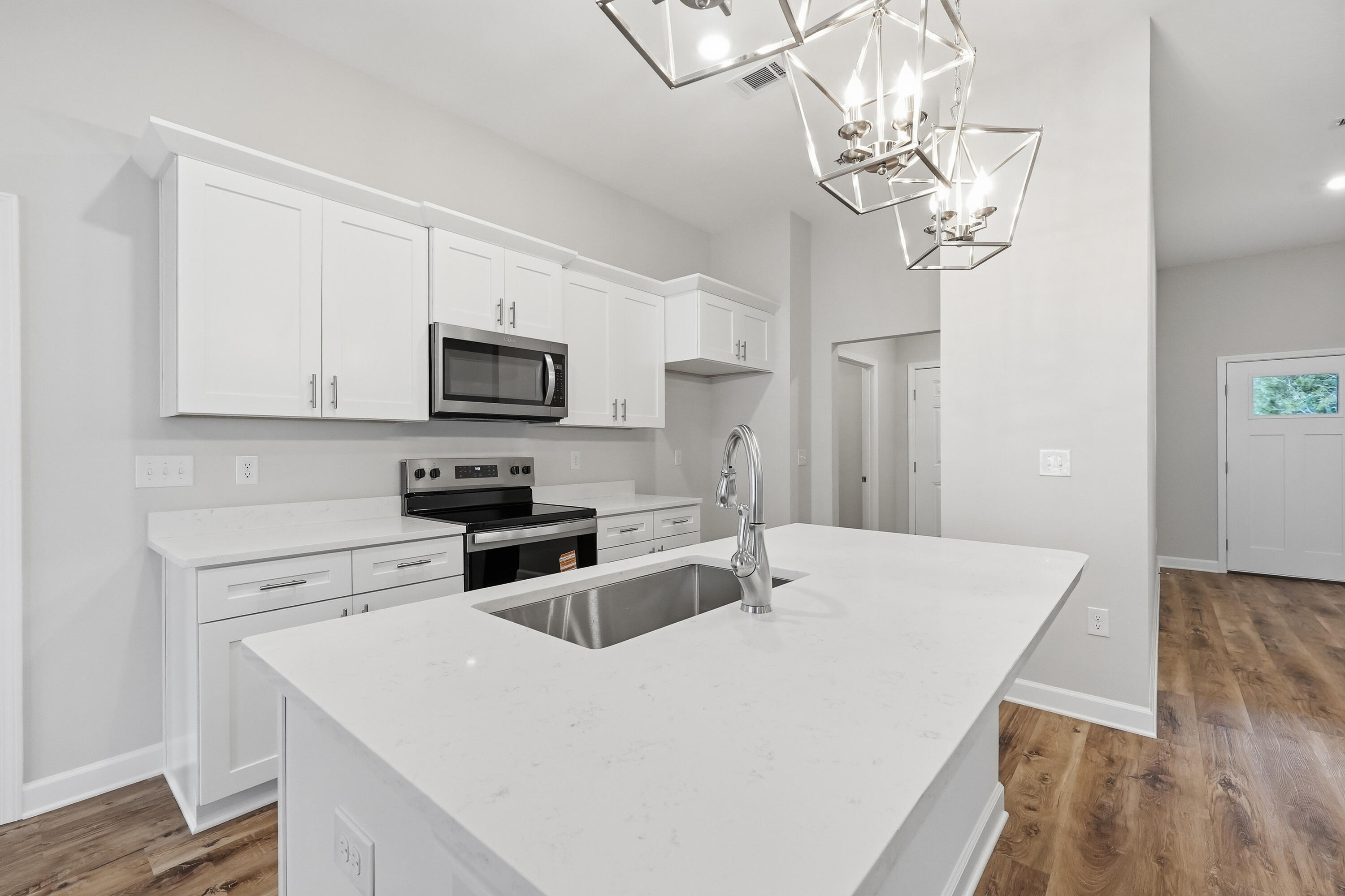 Modern white kitchen with a large island sink, stainless steel appliances, and geometric pendant lights.