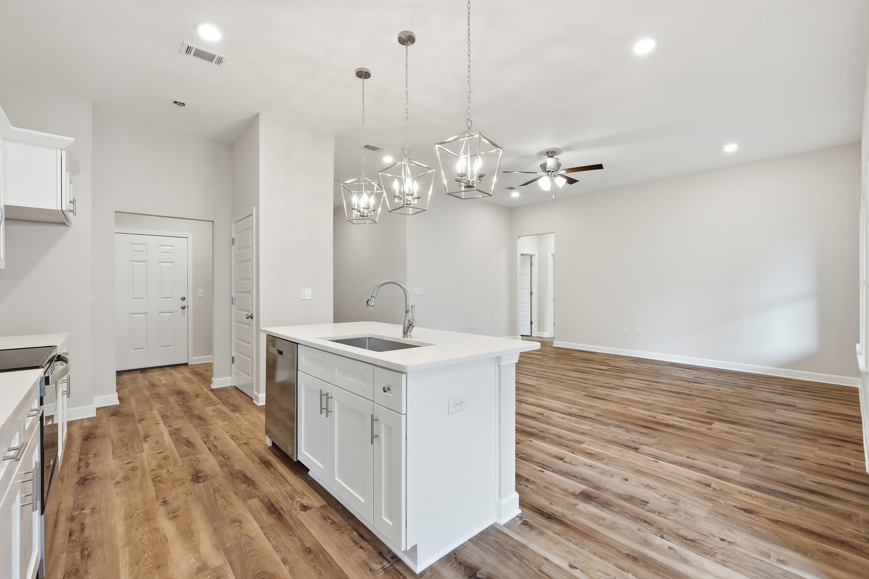 Unfurnished kitchen with a large white island, geometric pendant lights, and wood-look floors.