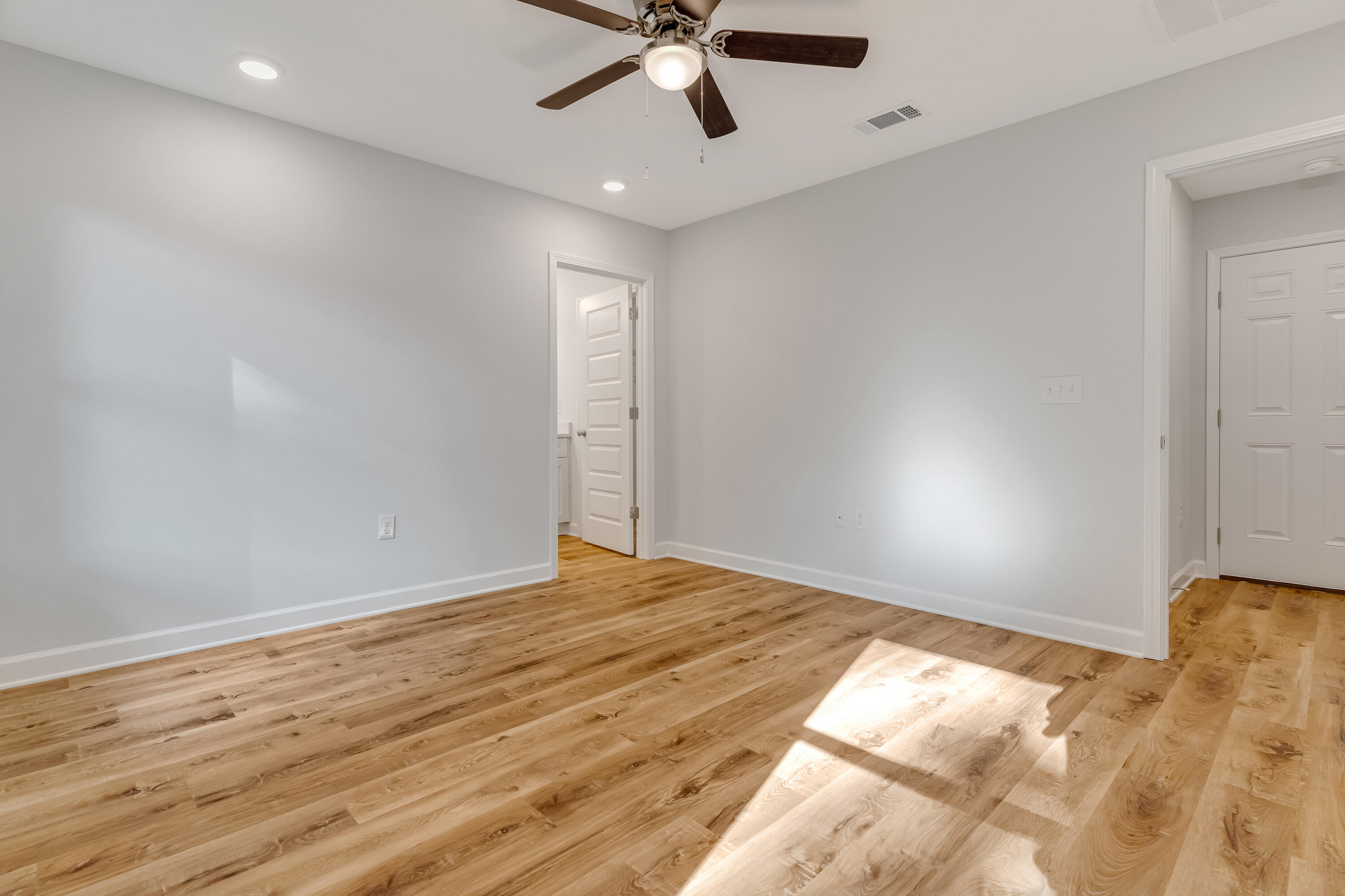 Empty bedroom with hardwood floors, a ceiling fan, and sunlight across the floor.