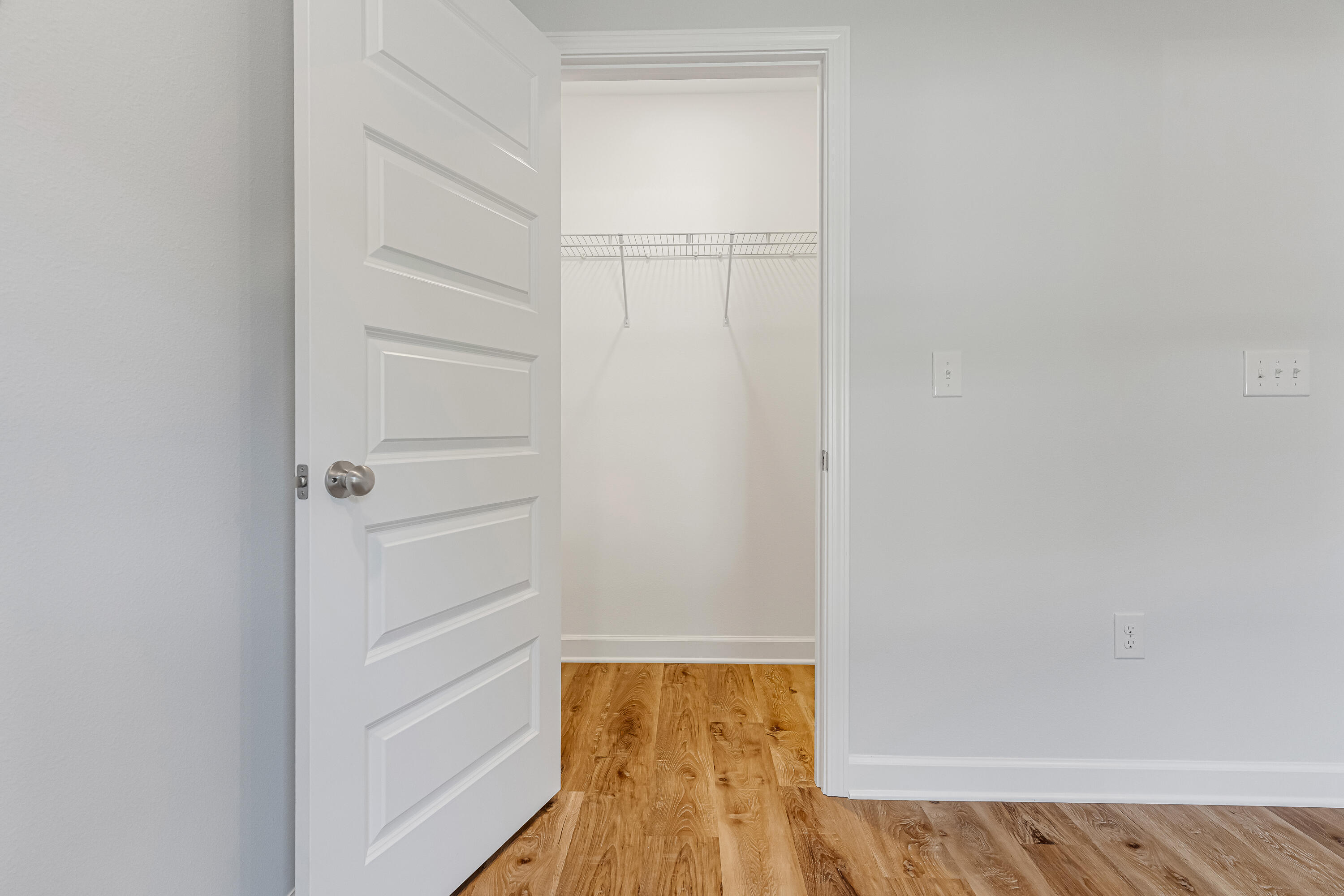 Empty walk-in closet with a white wire shelf and warm wood-look flooring