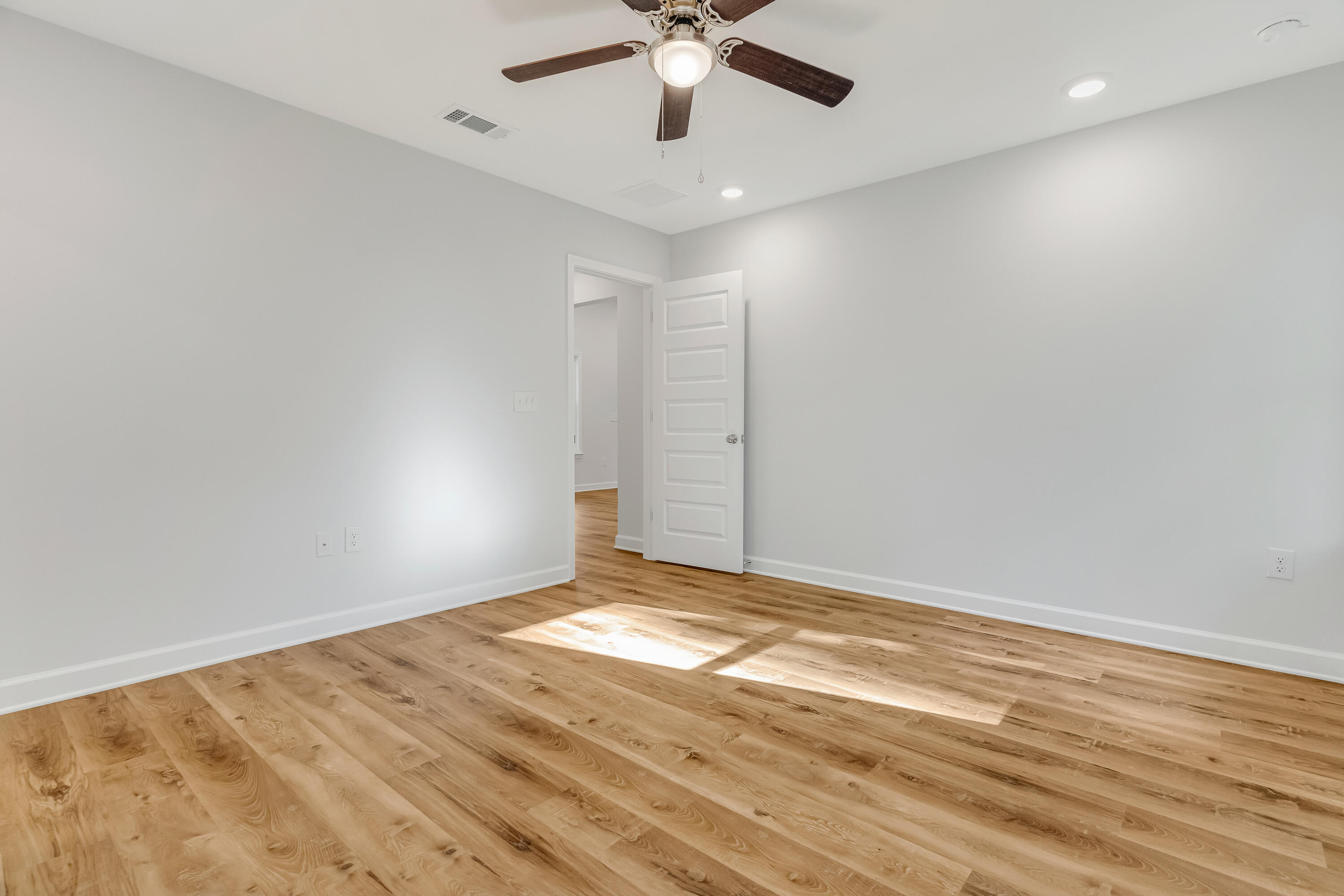 Empty room with wood-look flooring, a ceiling fan, and an open door to the hallway.