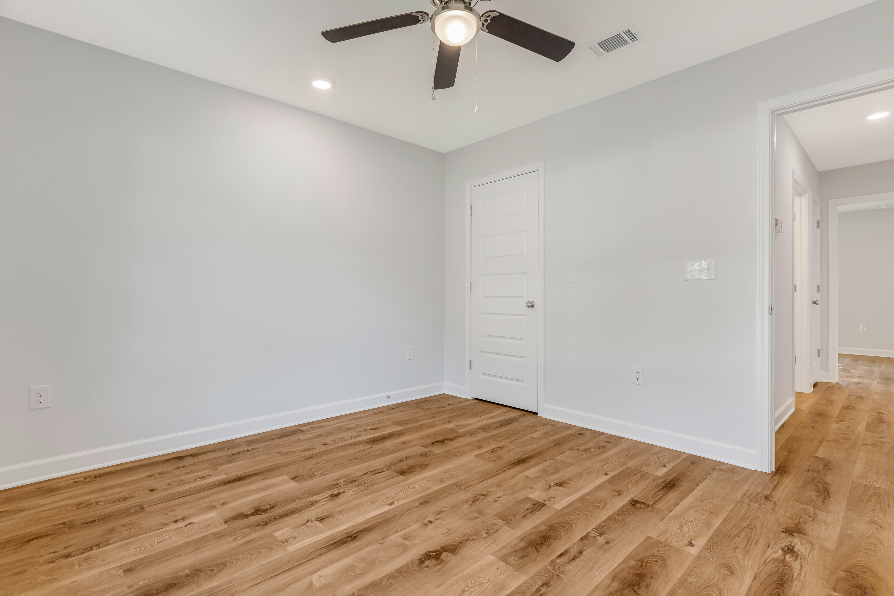 Empty room with wide-plank wood floors, gray walls, and a ceiling fan.