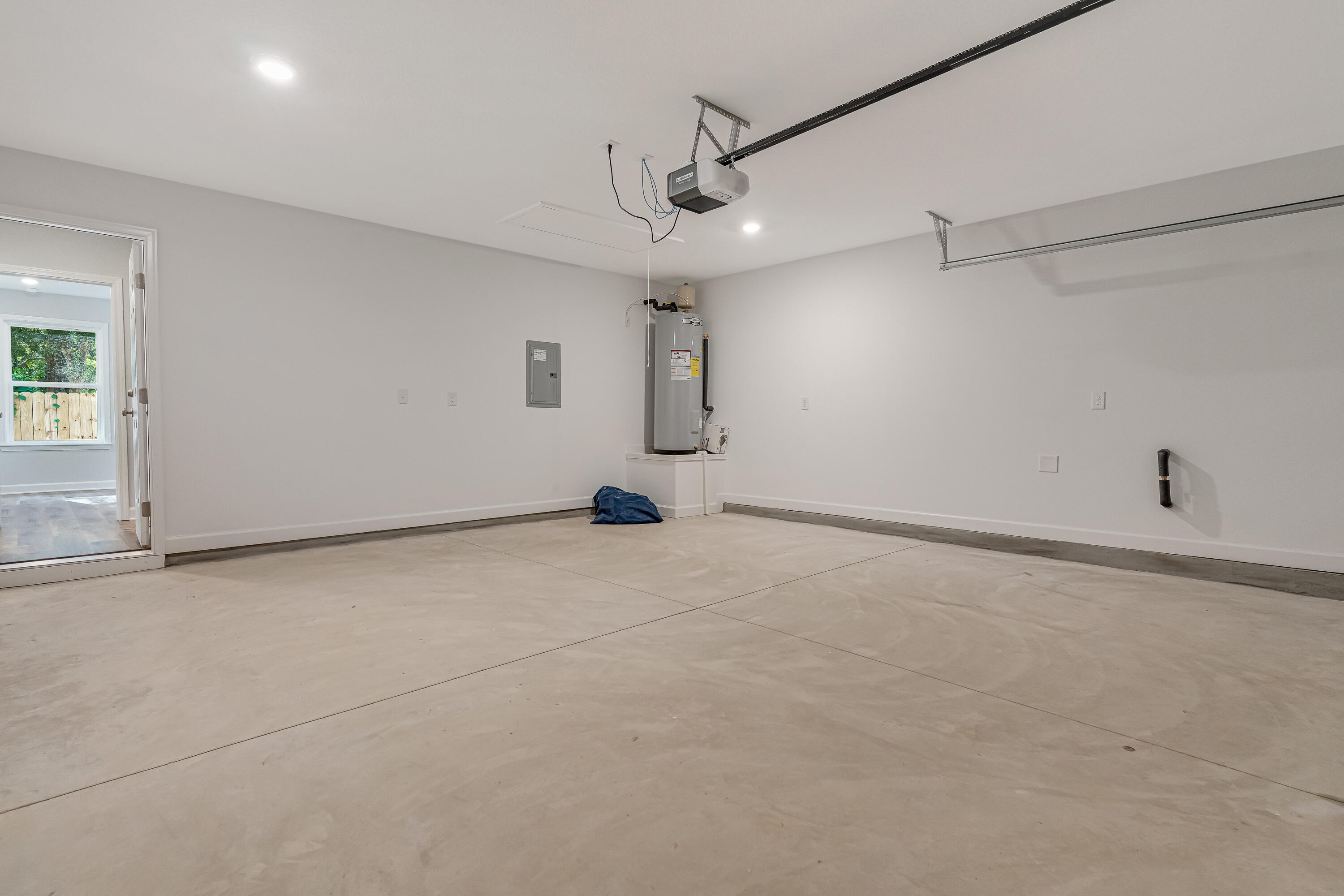 Empty garage with concrete floor, overhead door opener, and water heater.