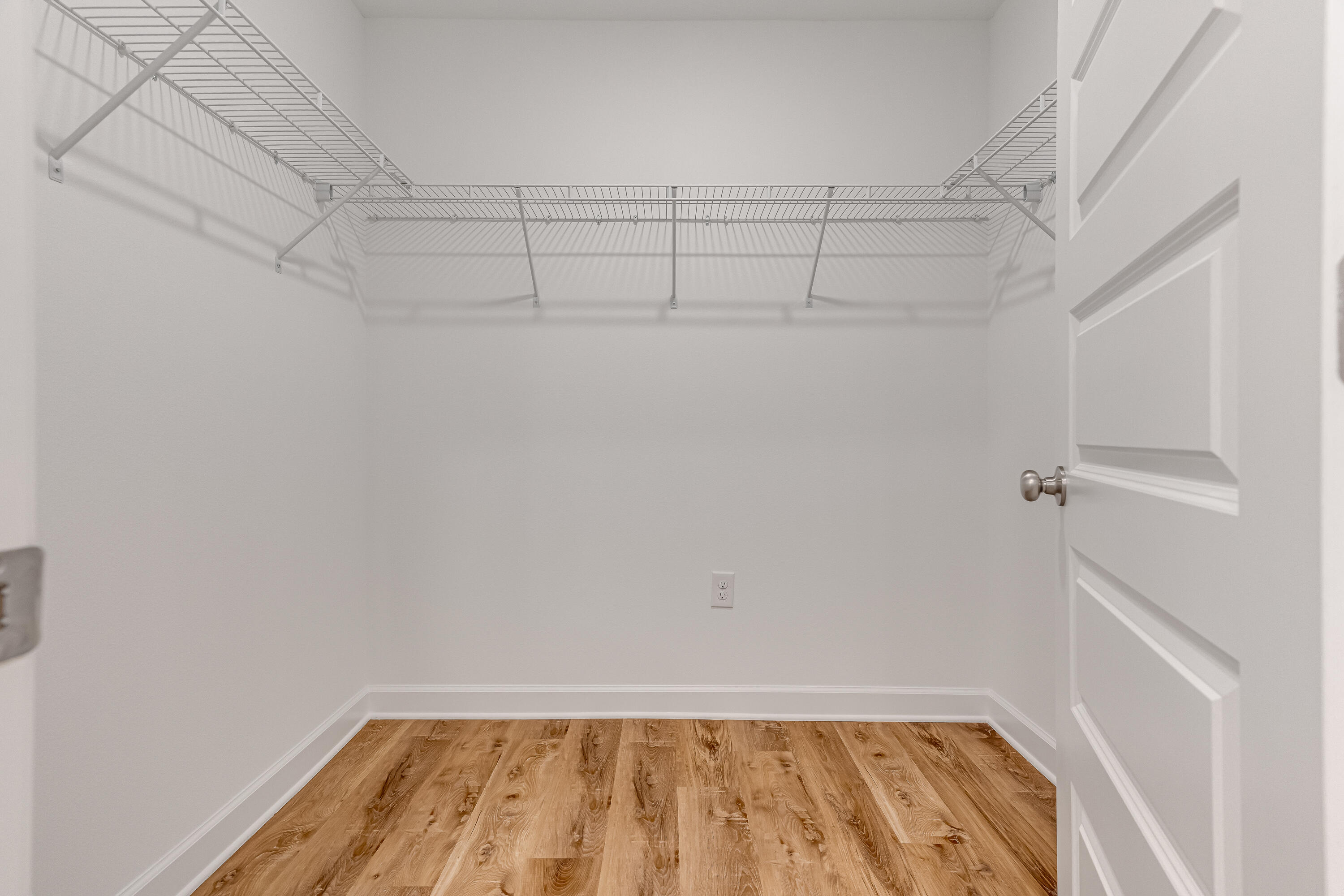 Walk-in closet with wraparound wire shelving and warm wood-look flooring.