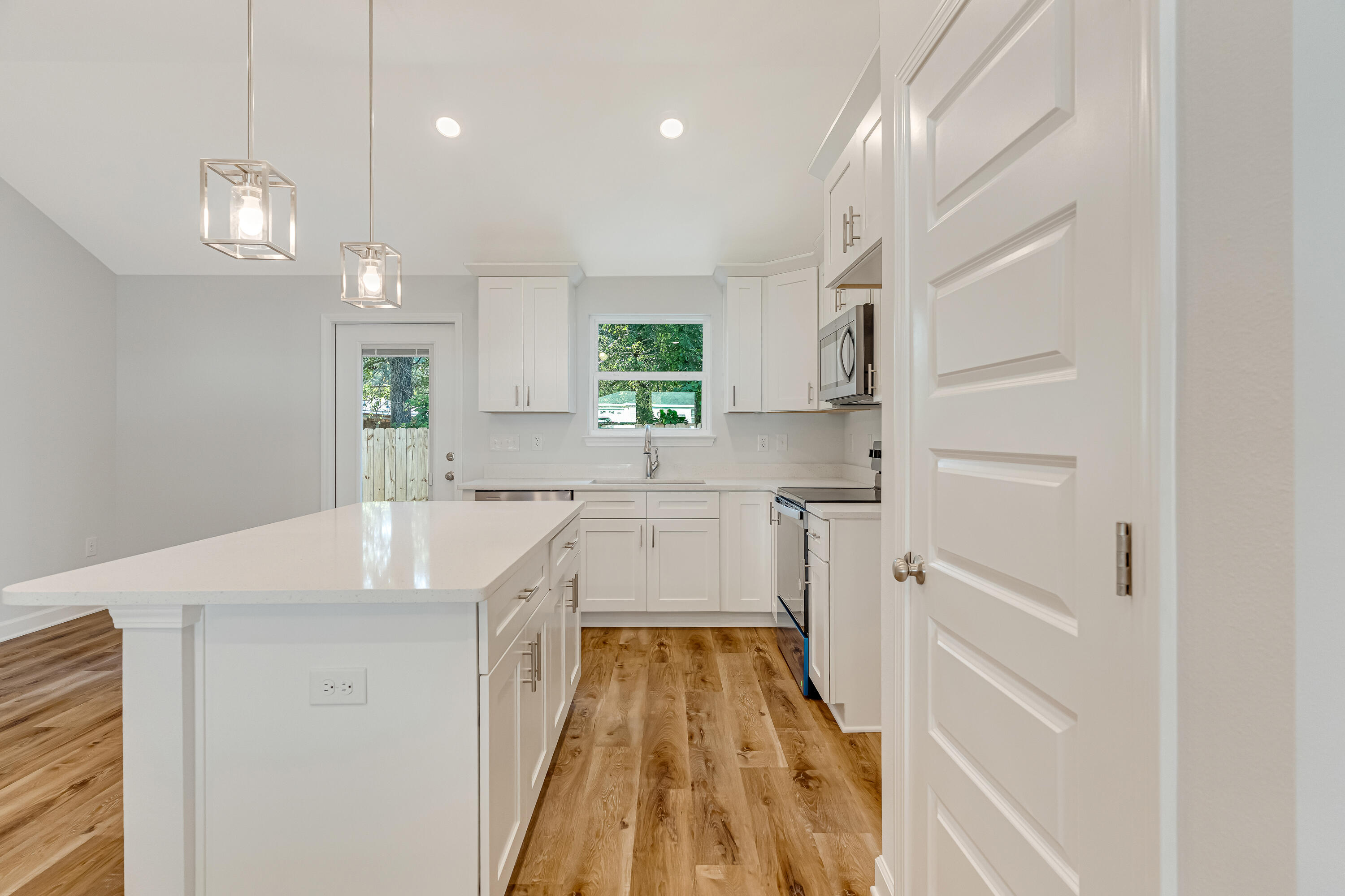 Bright white kitchen with a large island, stainless steel appliances, and warm wood-look floors.