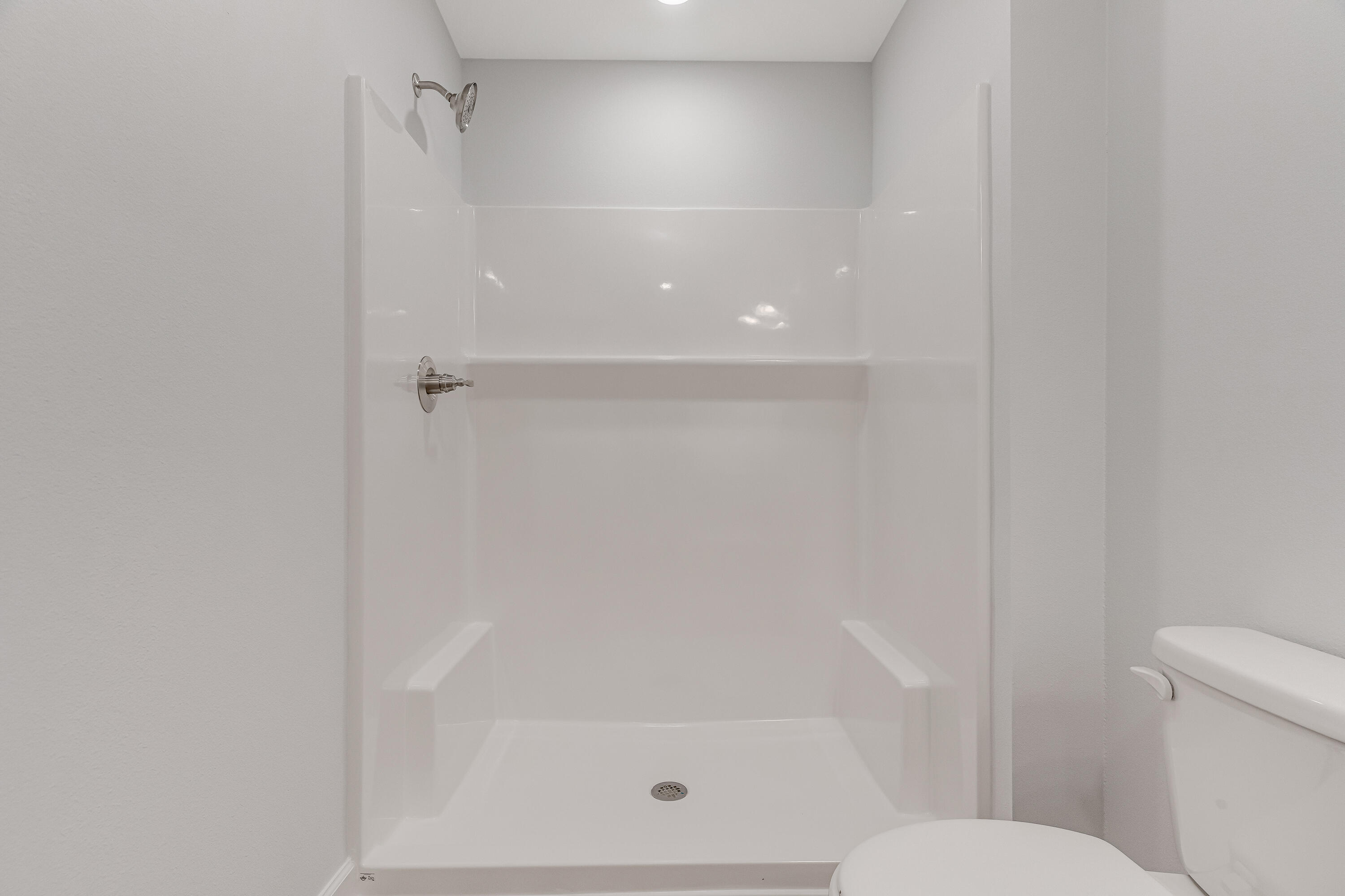 White walk-in shower with a built-in shelf and chrome fixtures beside a toilet.