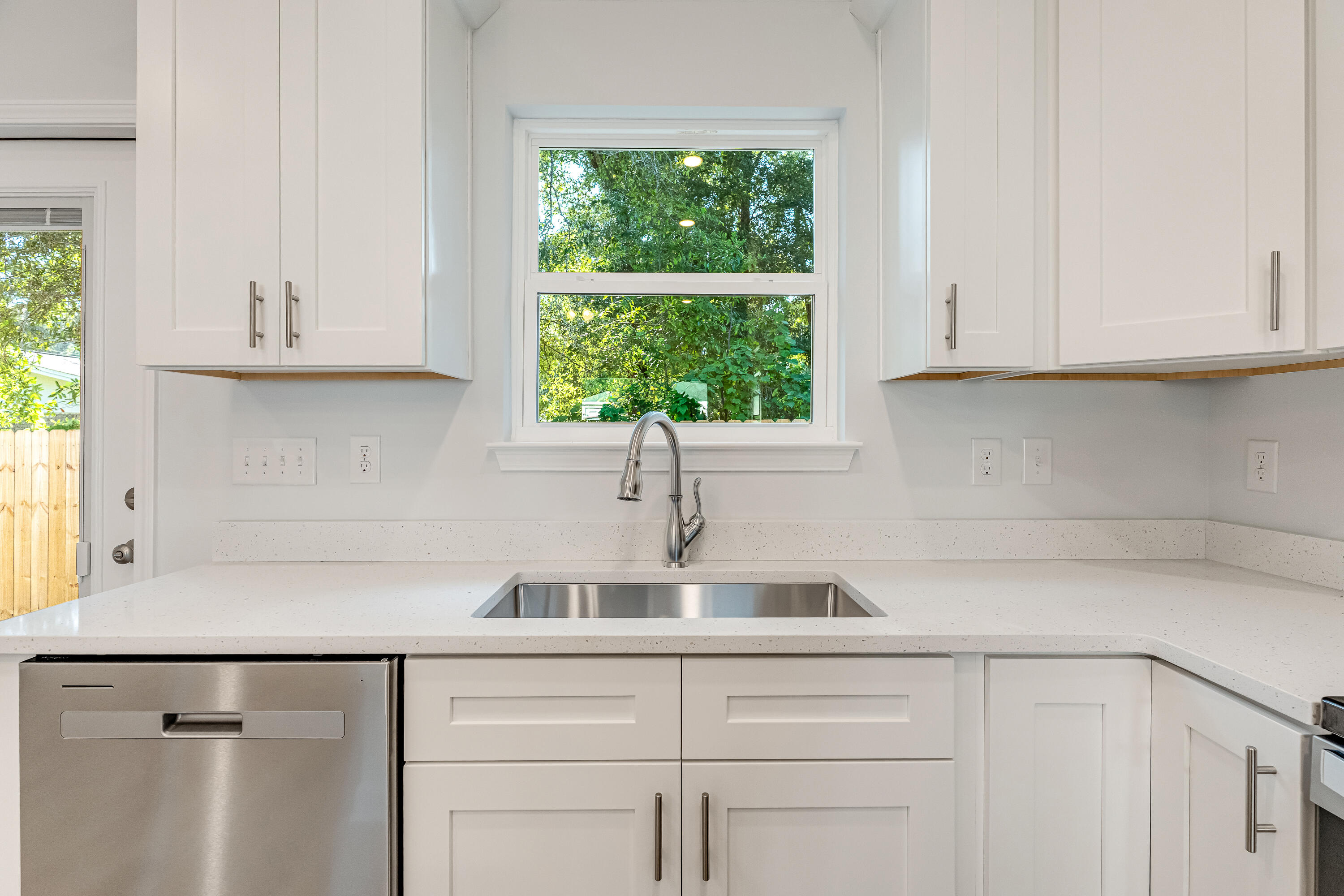 Bright kitchen with white cabinets, a stainless-steel sink, and a window facing leafy trees.