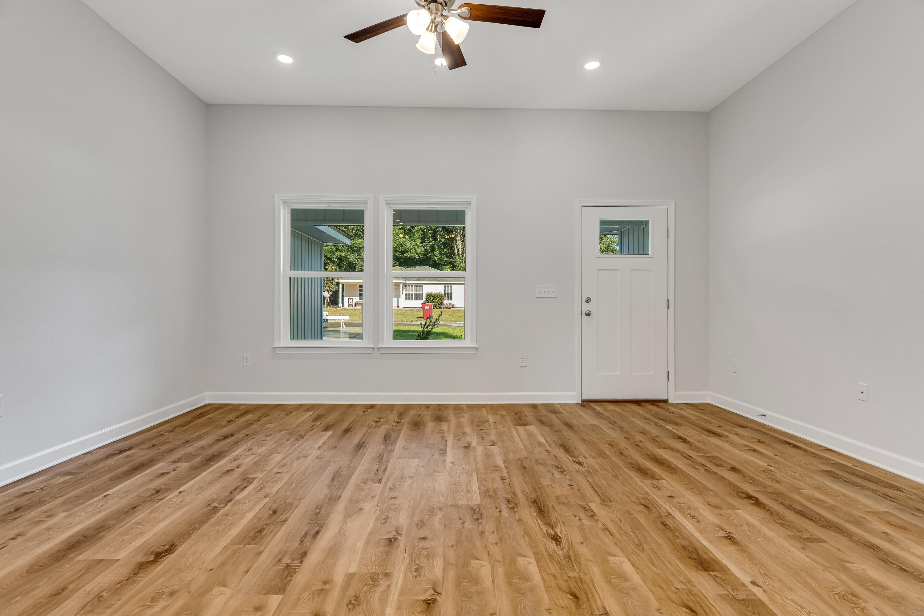 Empty room with warm wood-look flooring, paired windows, and a ceiling fan.