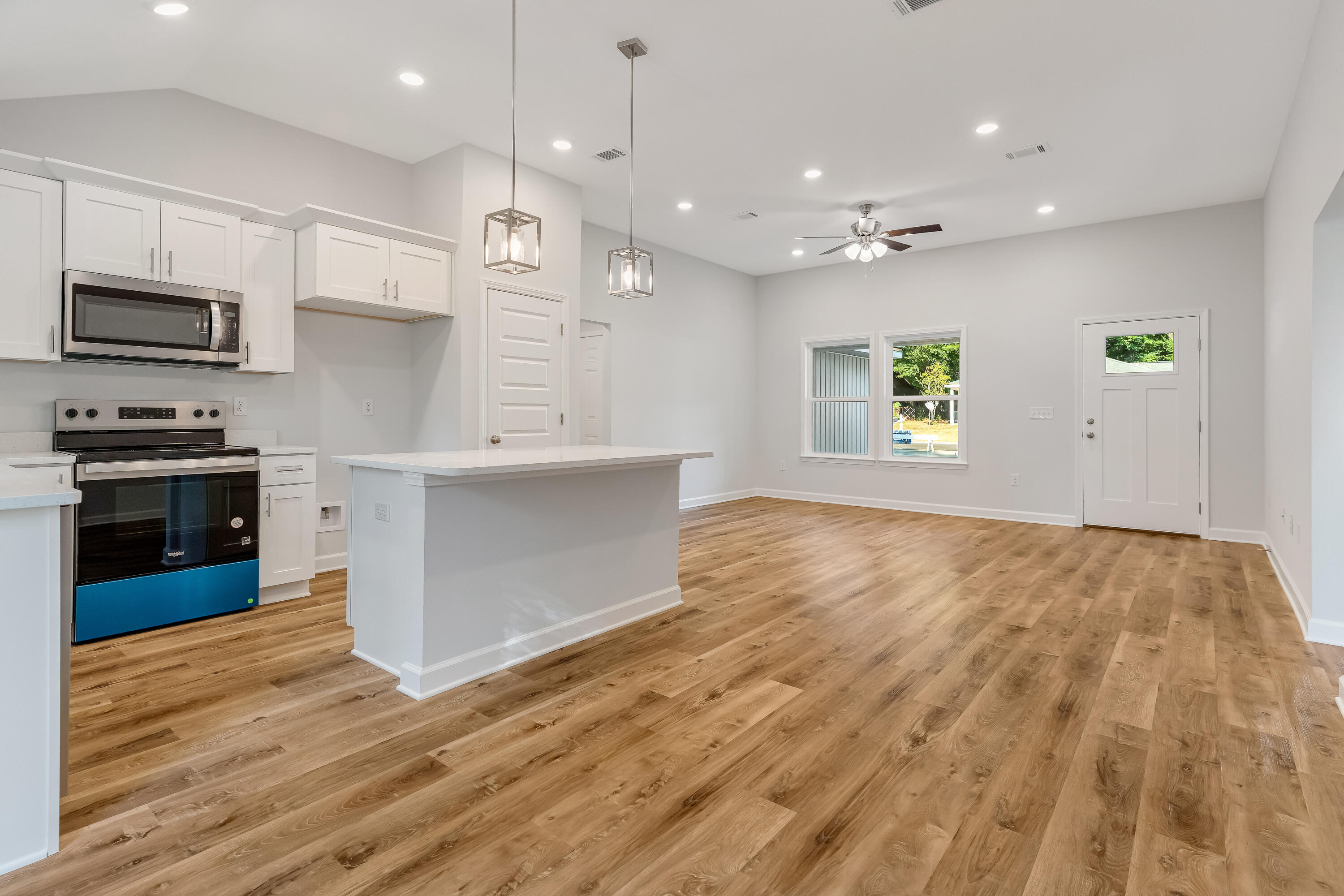 Open-plan kitchen and living area with a white island, shaker cabinets, and warm wood-look floors.