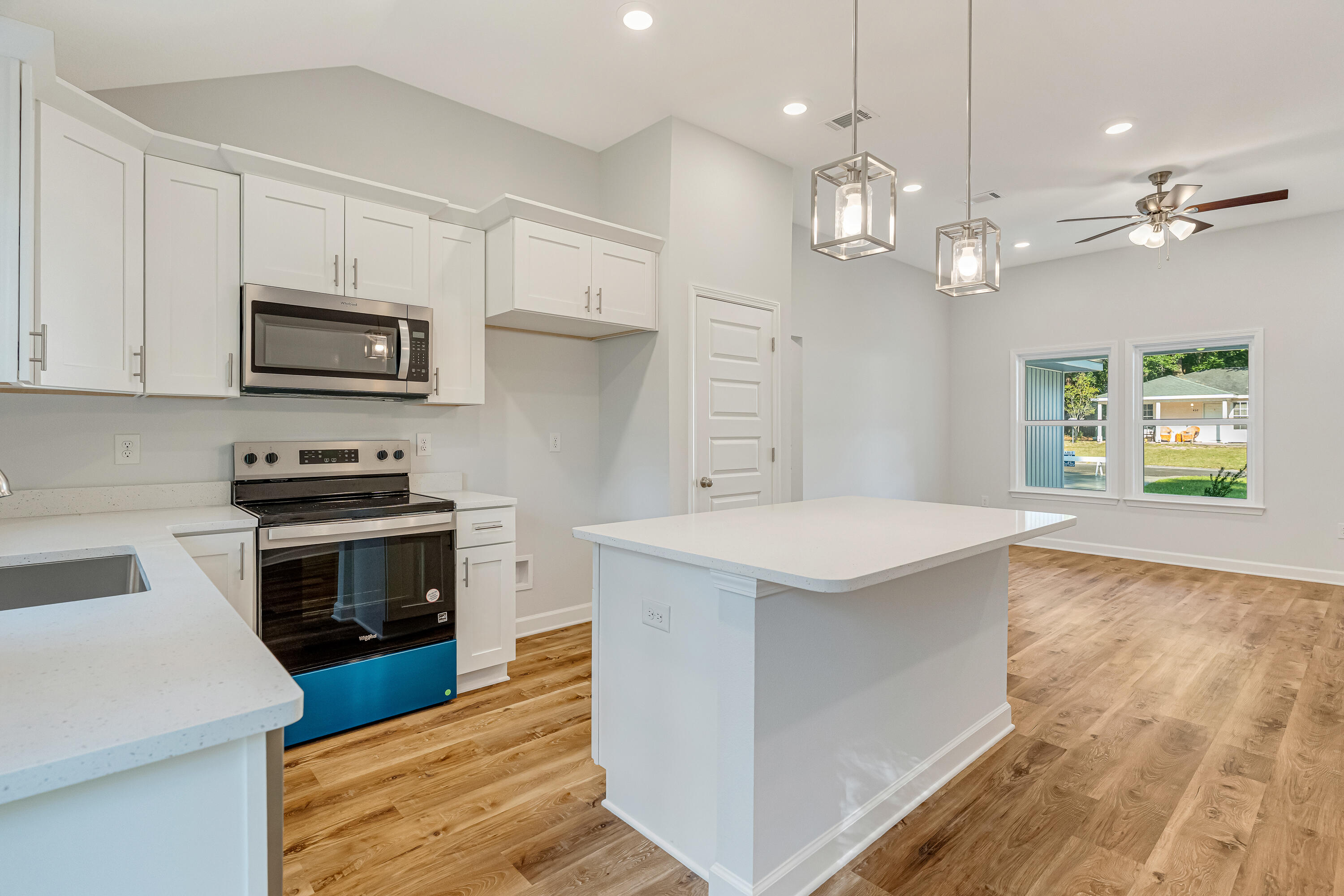 Vacant kitchen with a large white island, stainless steel appliances, and warm wood-look flooring.