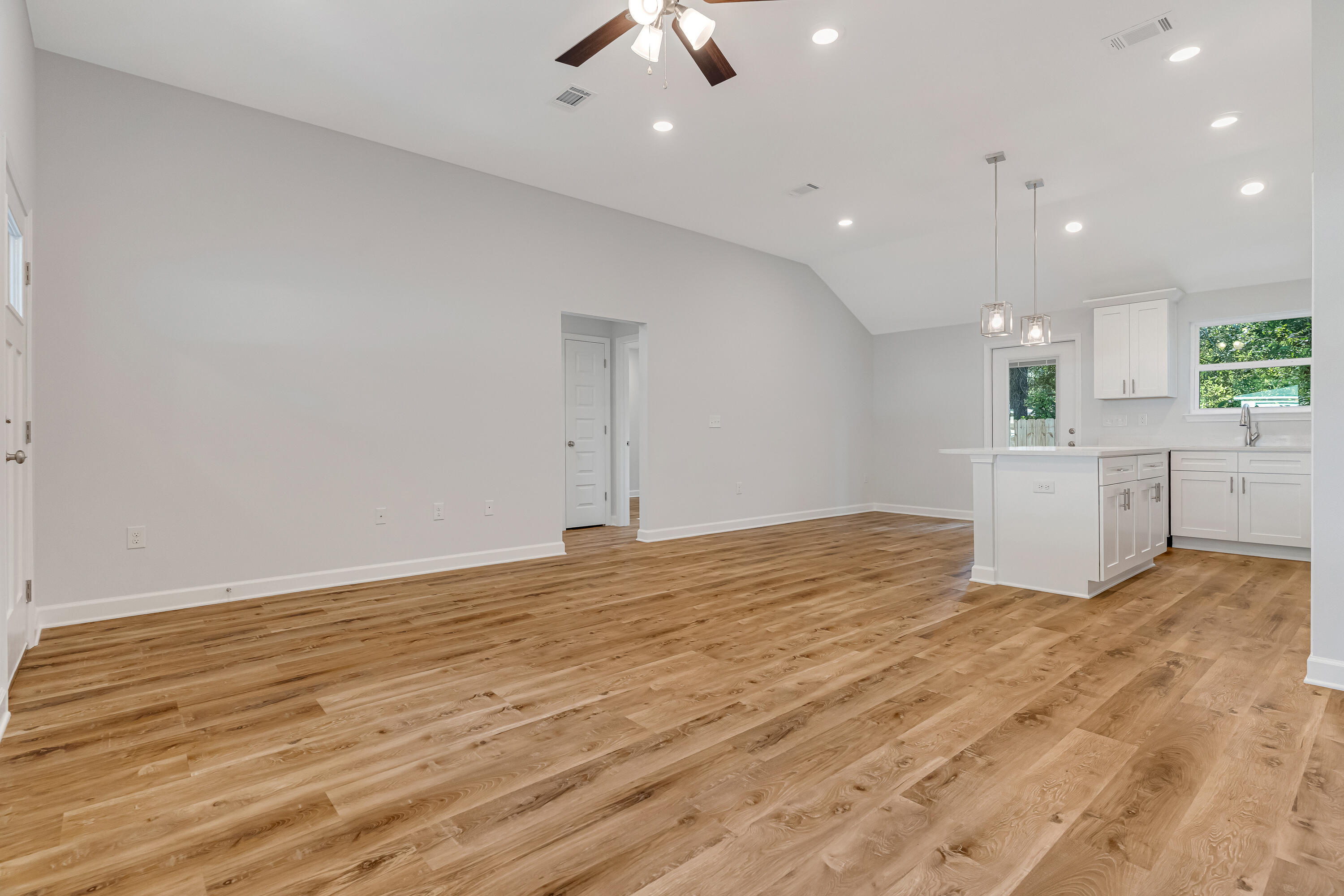 Open-plan kitchen and living area with a white island, warm wood-look floors, and vaulted ceiling.