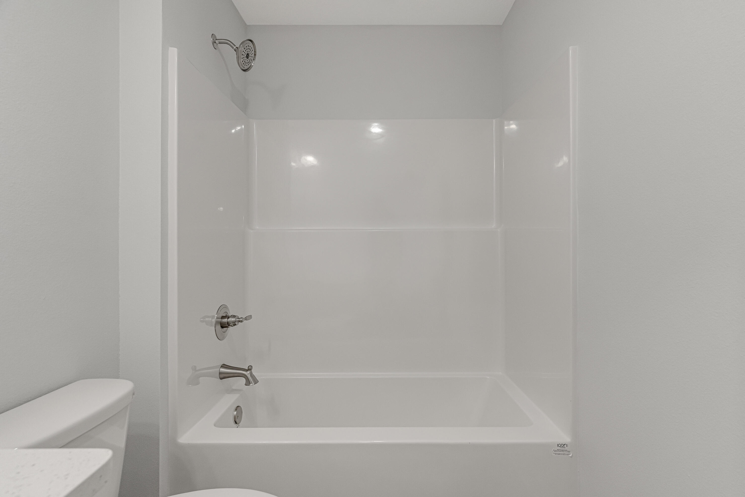 White bathtub and shower with chrome fixtures beside a partially visible toilet.
