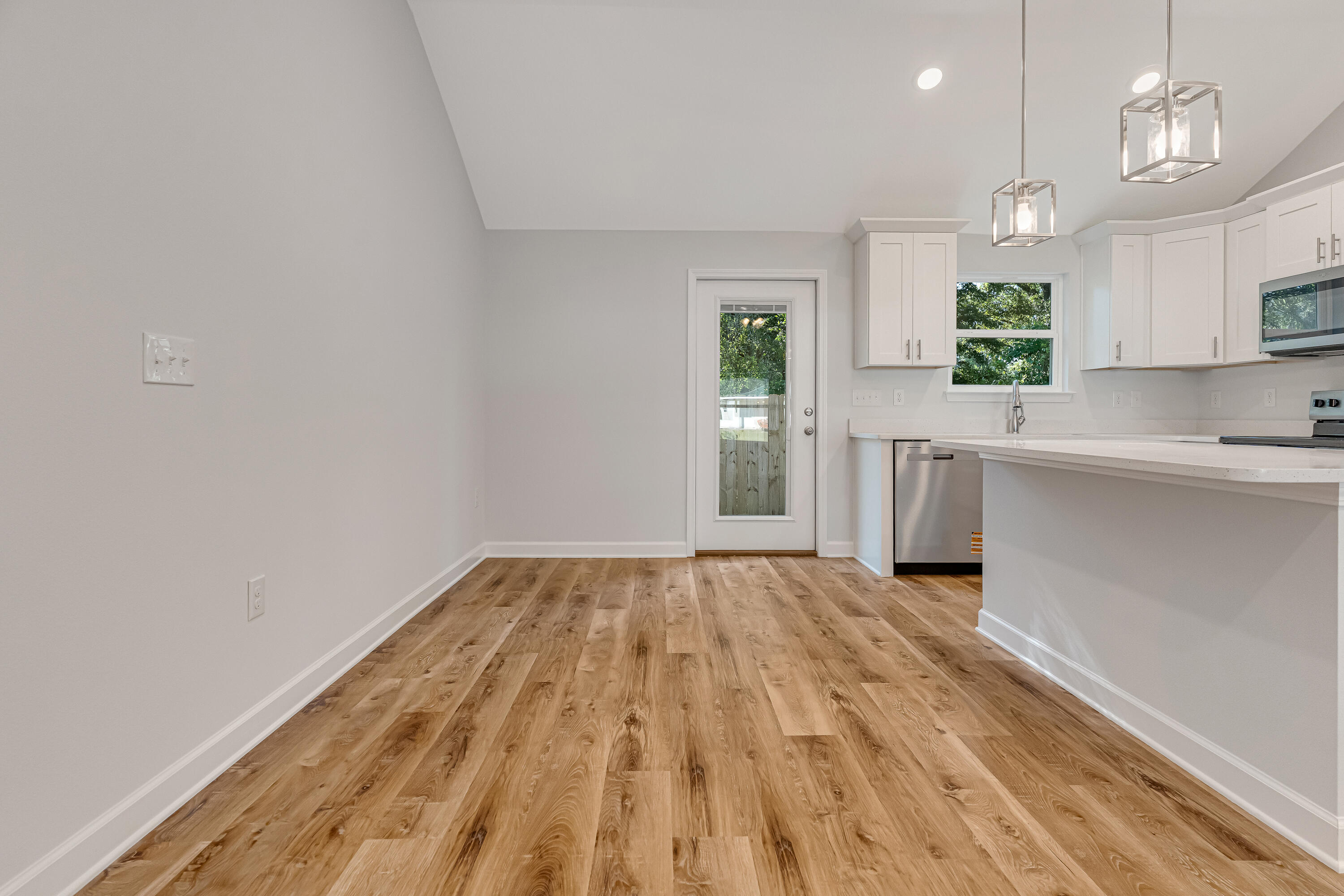 Vacant kitchen with white cabinets, stainless steel appliances, wood-look flooring, and a glass-paneled back door.