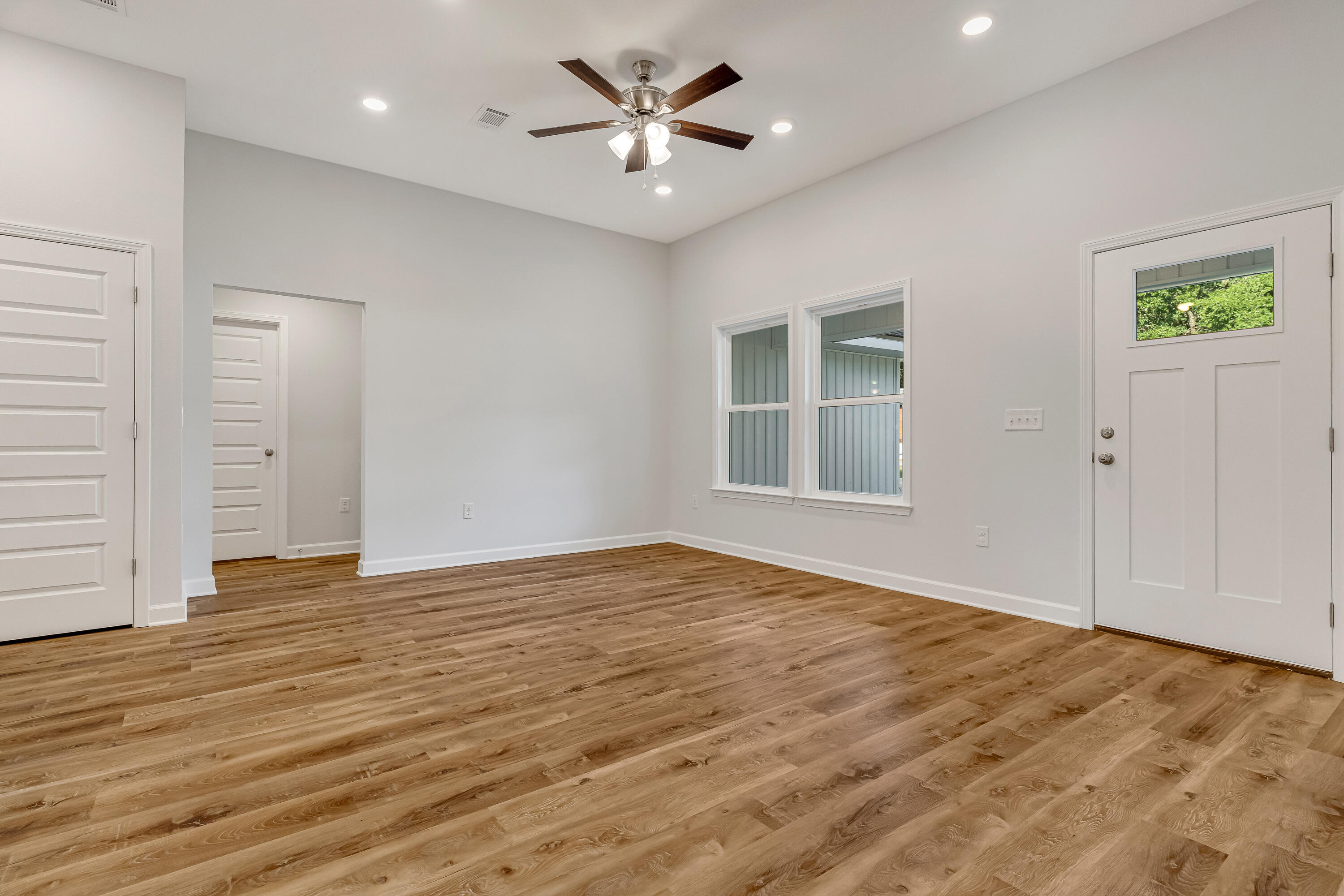 Vacant room with wood-look flooring, a ceiling fan, two windows, and an exterior door.