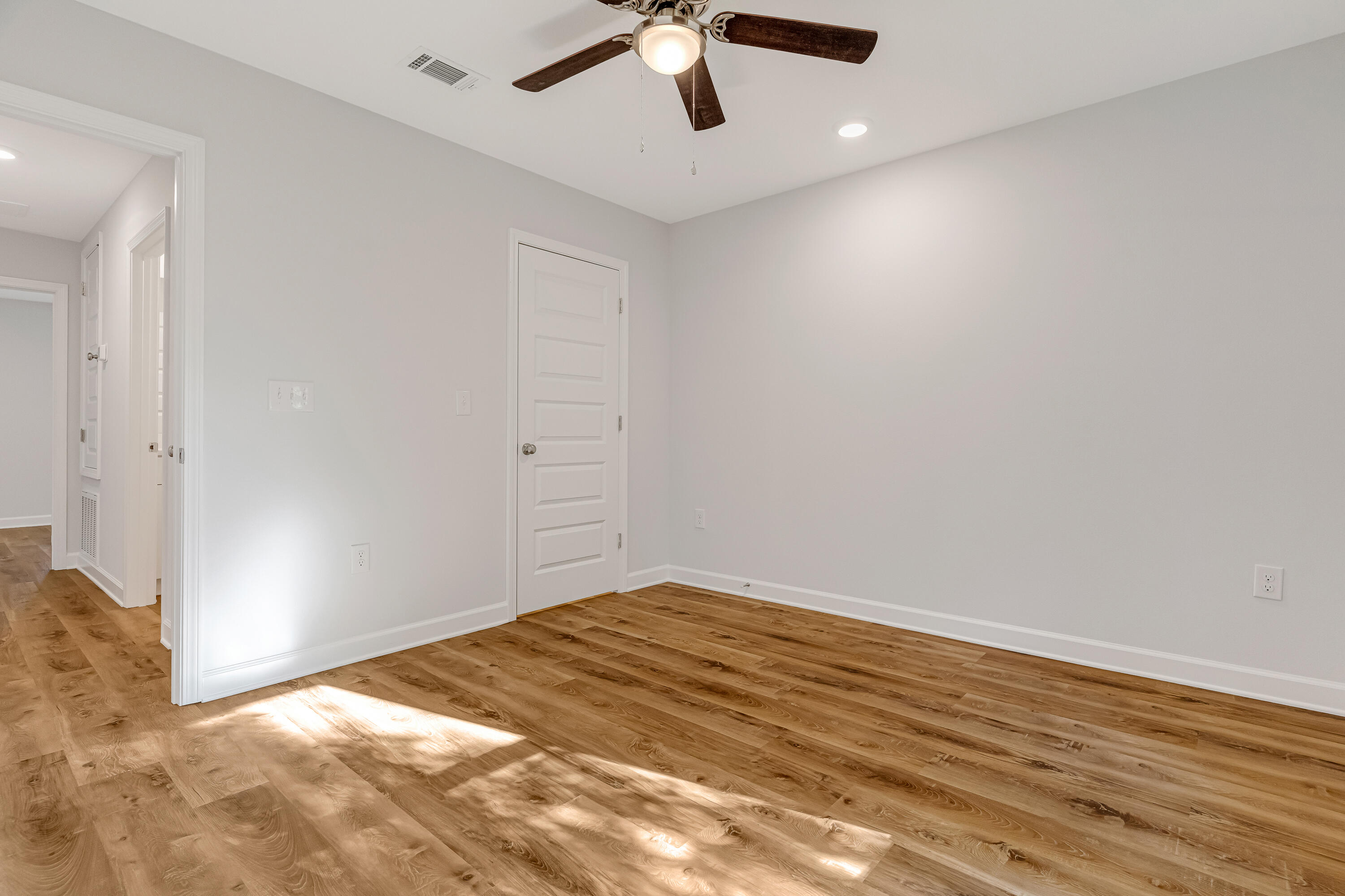 Empty room with wood-look plank flooring, gray walls, and a ceiling fan.