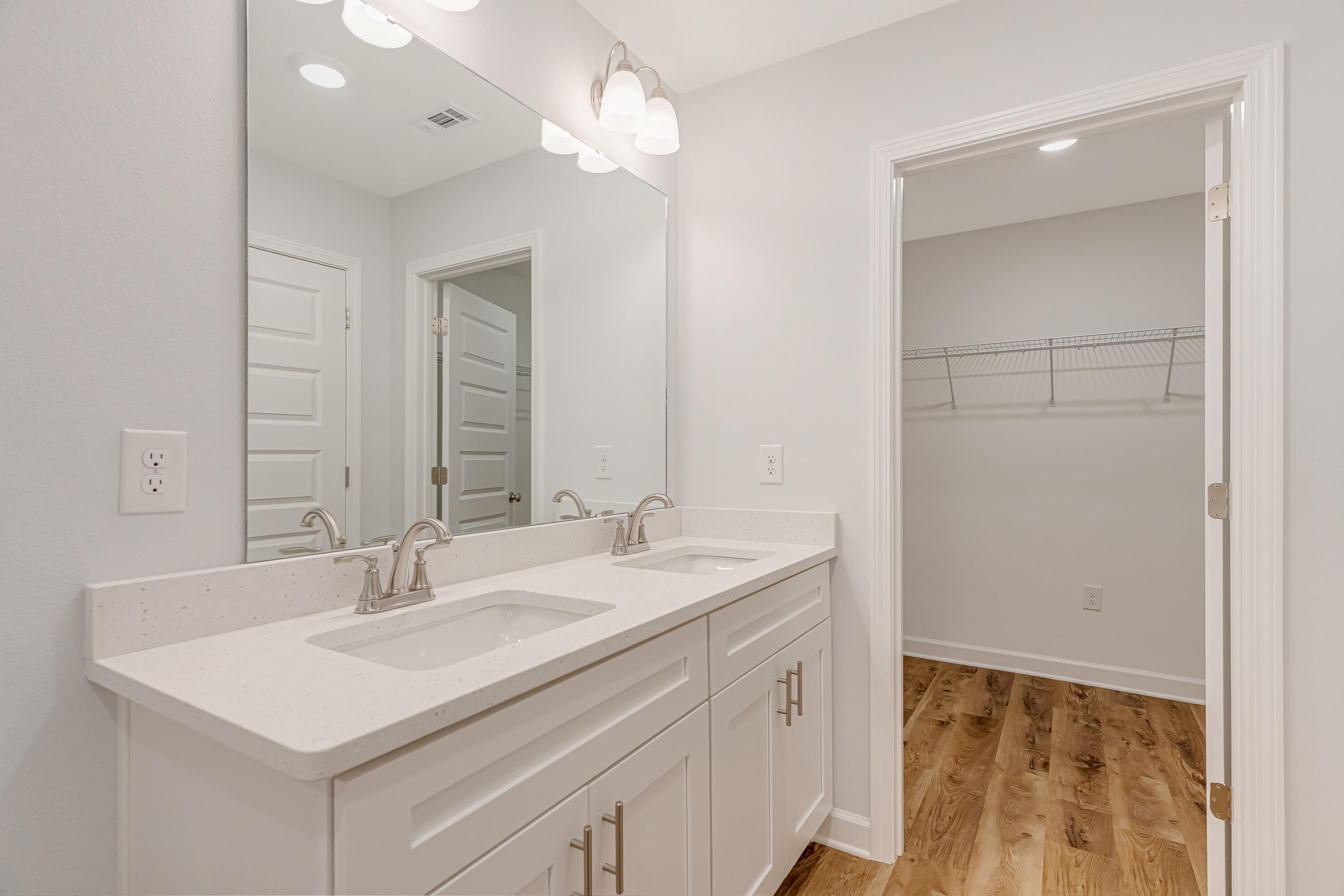 Bathroom with a white double-sink vanity and open closet with wire shelving.