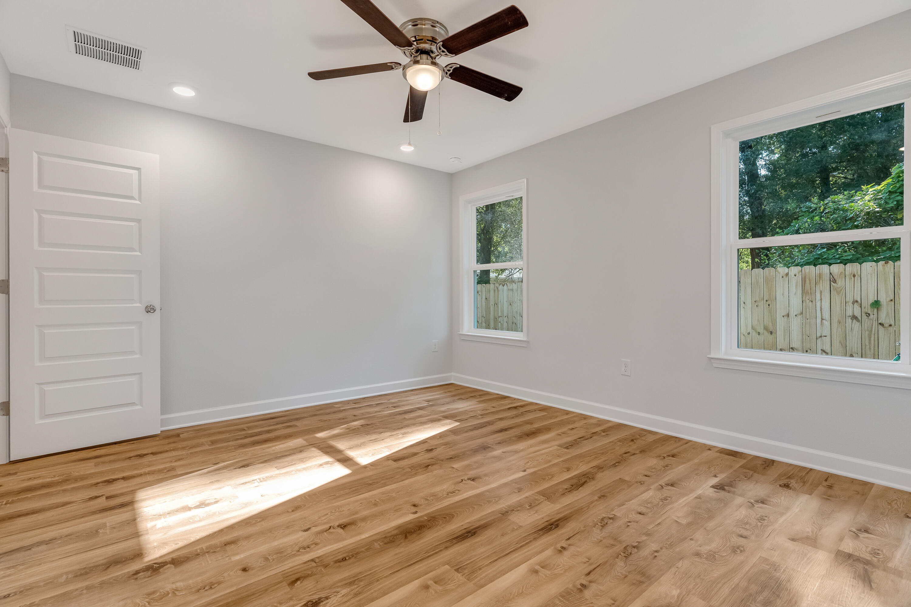 Empty room with wood-look floors, two windows, and a ceiling fan.