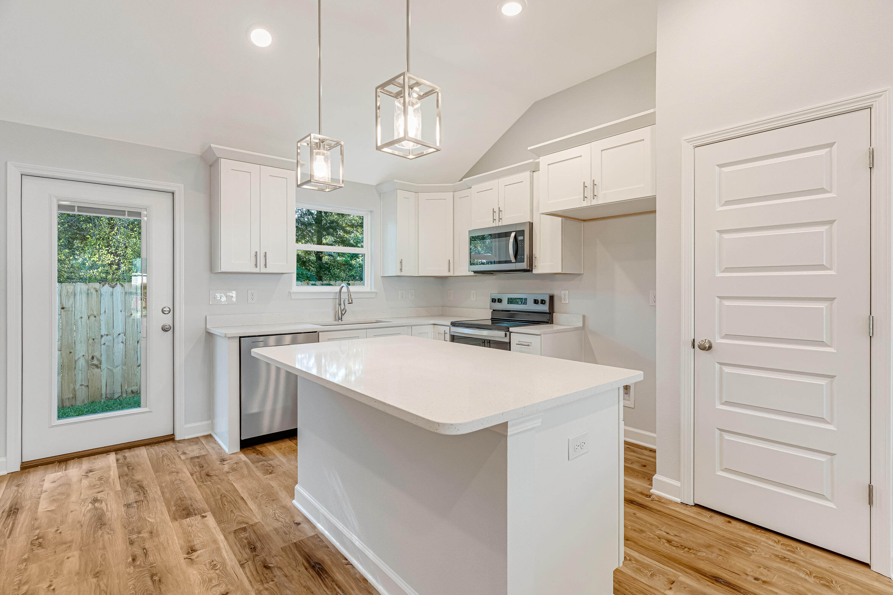 Bright kitchen with a large white island, shaker cabinets, and stainless steel appliances.