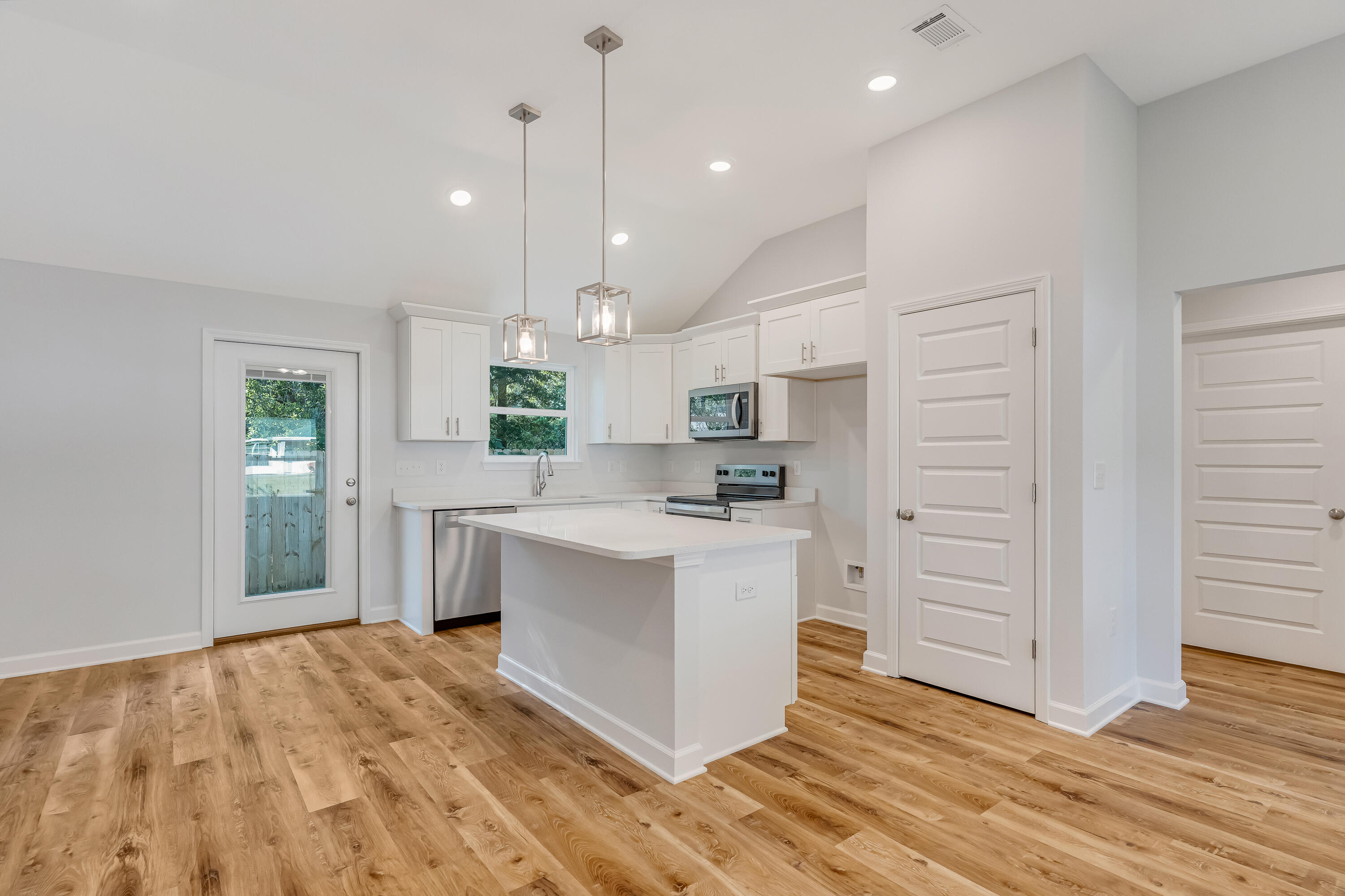 Kitchen with white cabinets, stainless steel appliances, a central island, and warm wood-look flooring.