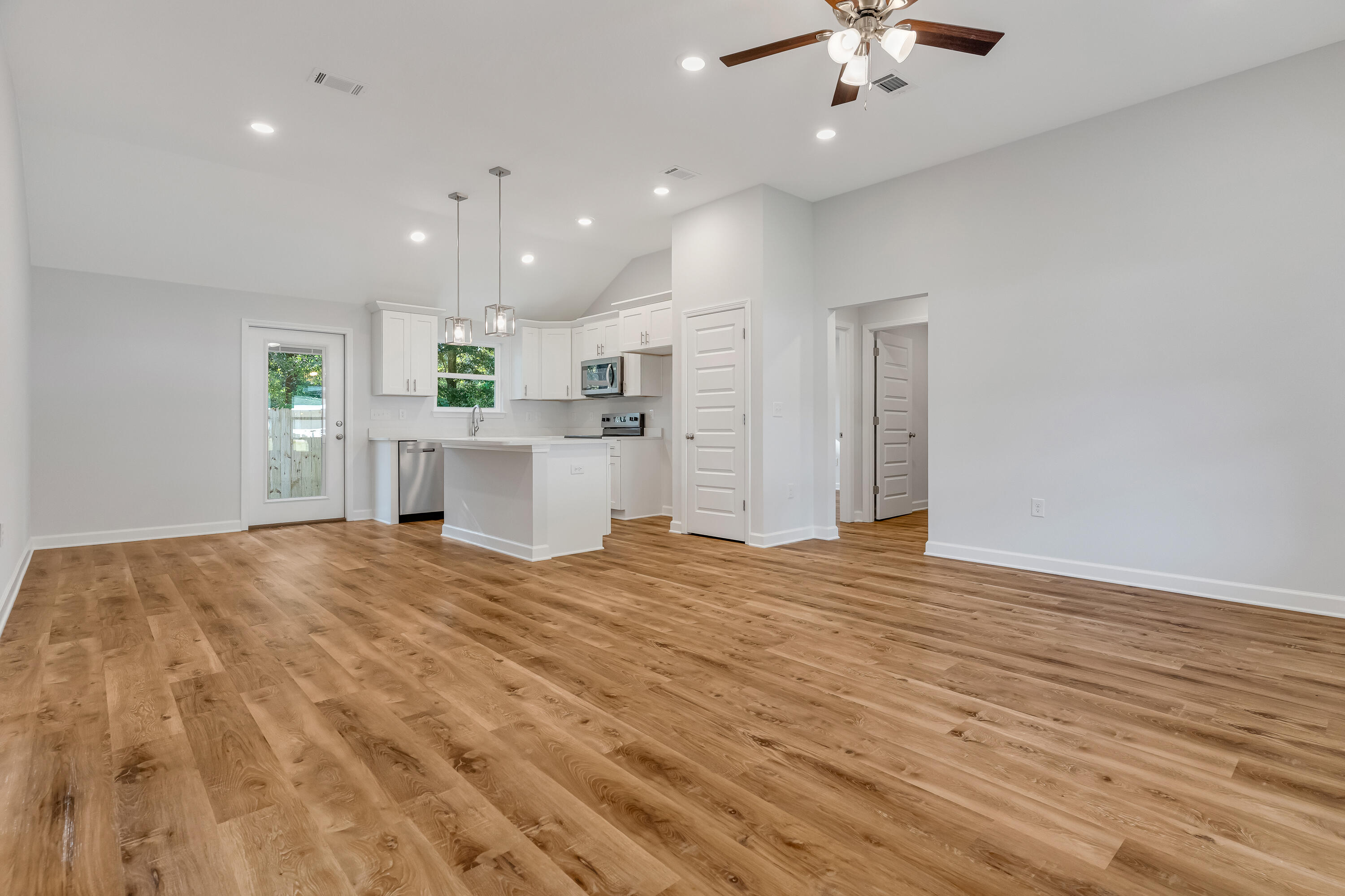 Open-plan kitchen and living area with white cabinets, an island, and warm wood-look floors.