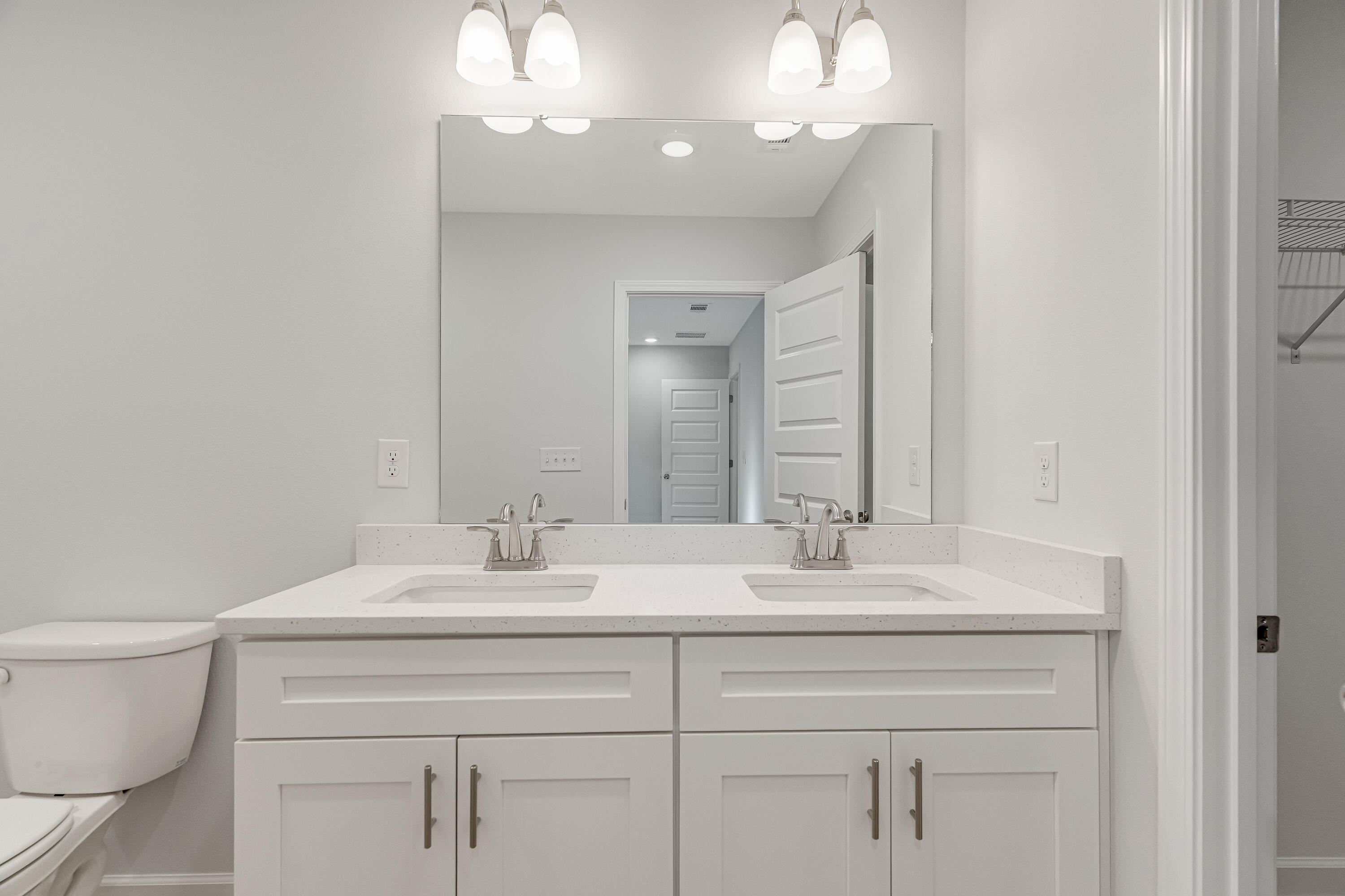Bathroom with a white double-sink vanity, large mirror, and toilet.