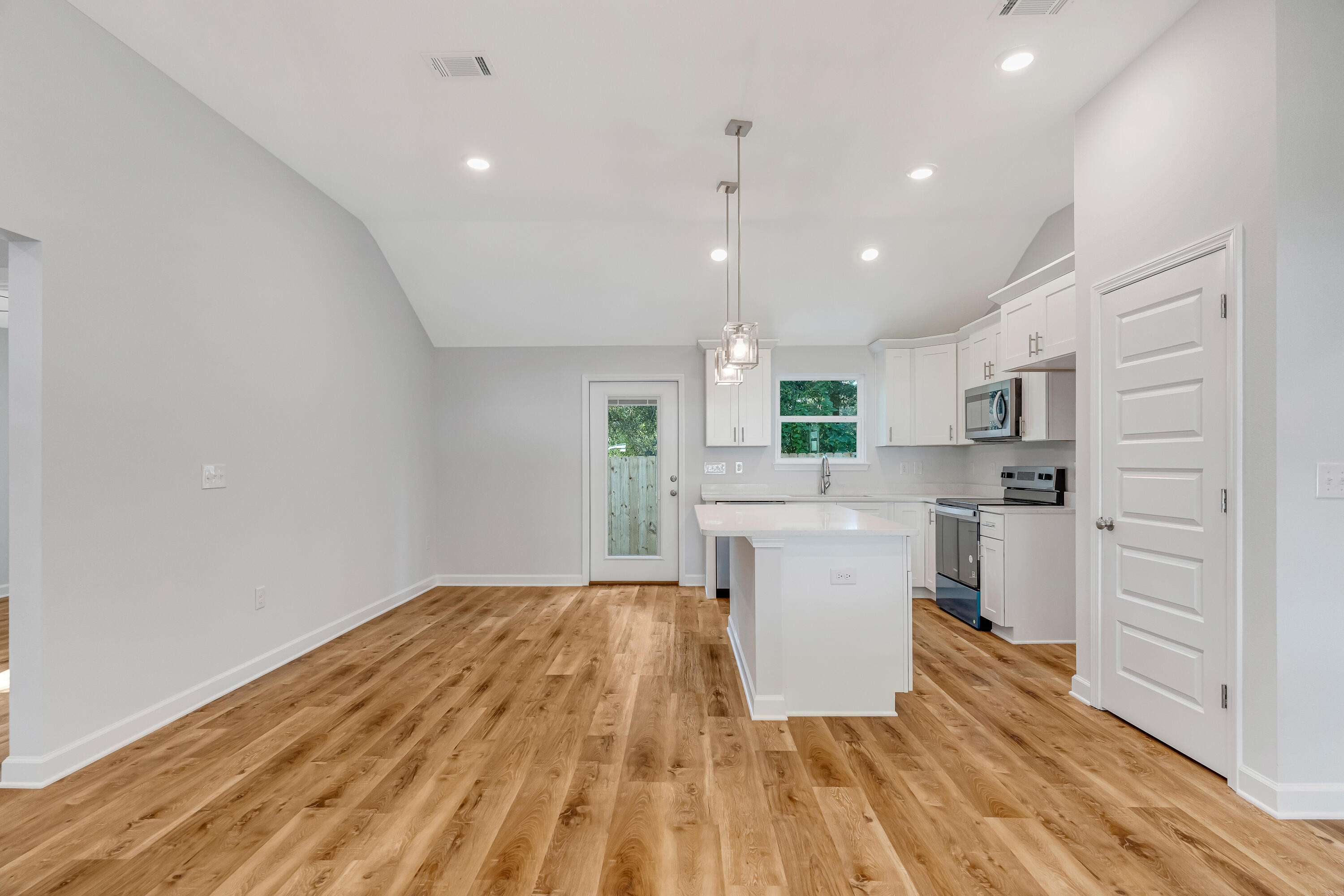 Open kitchen with white cabinets, a central island, stainless appliances, and warm wood-look flooring.