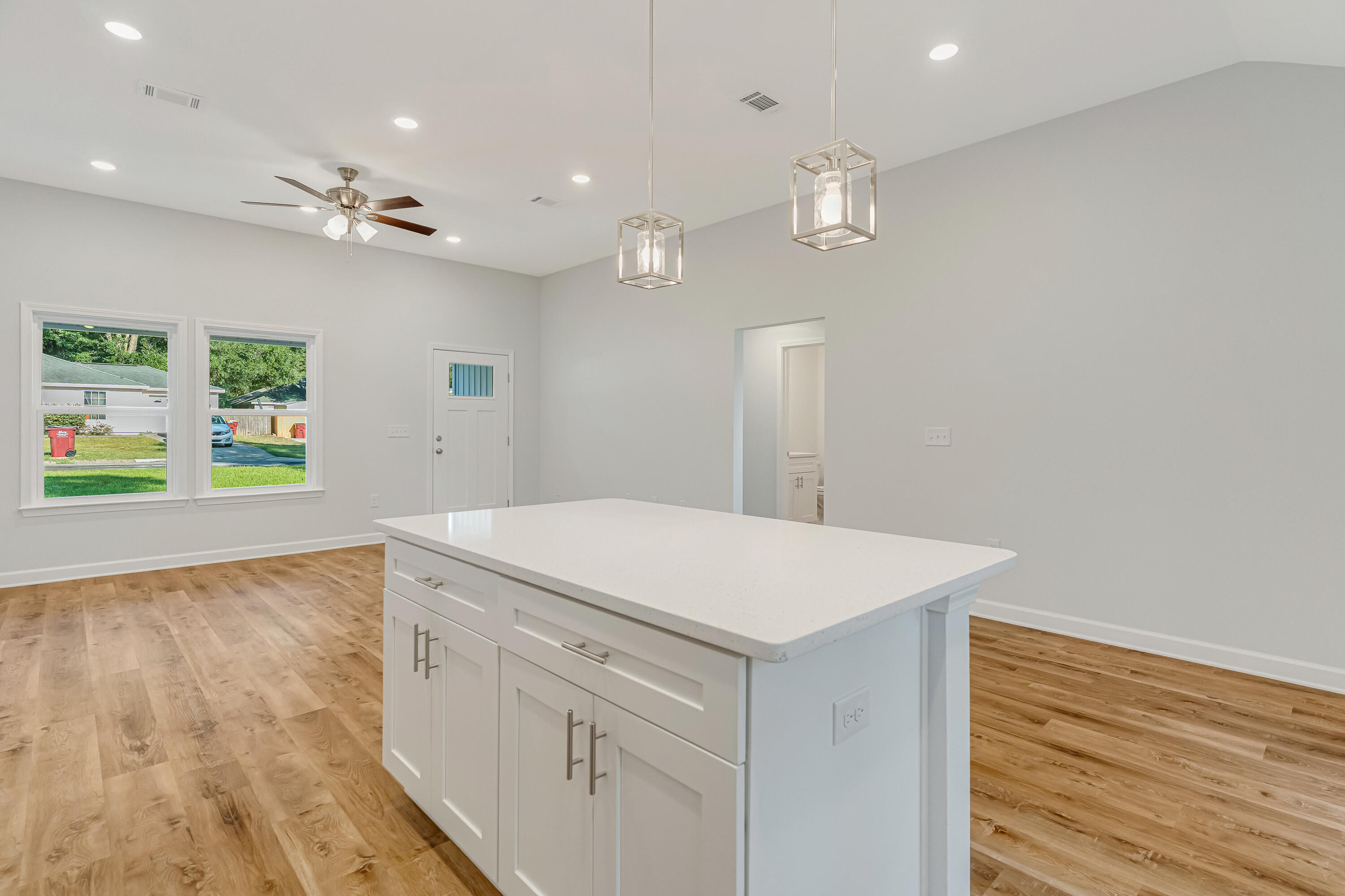 Vacant kitchen with a large white island, wood-look floors, and two windows overlooking a green lawn.