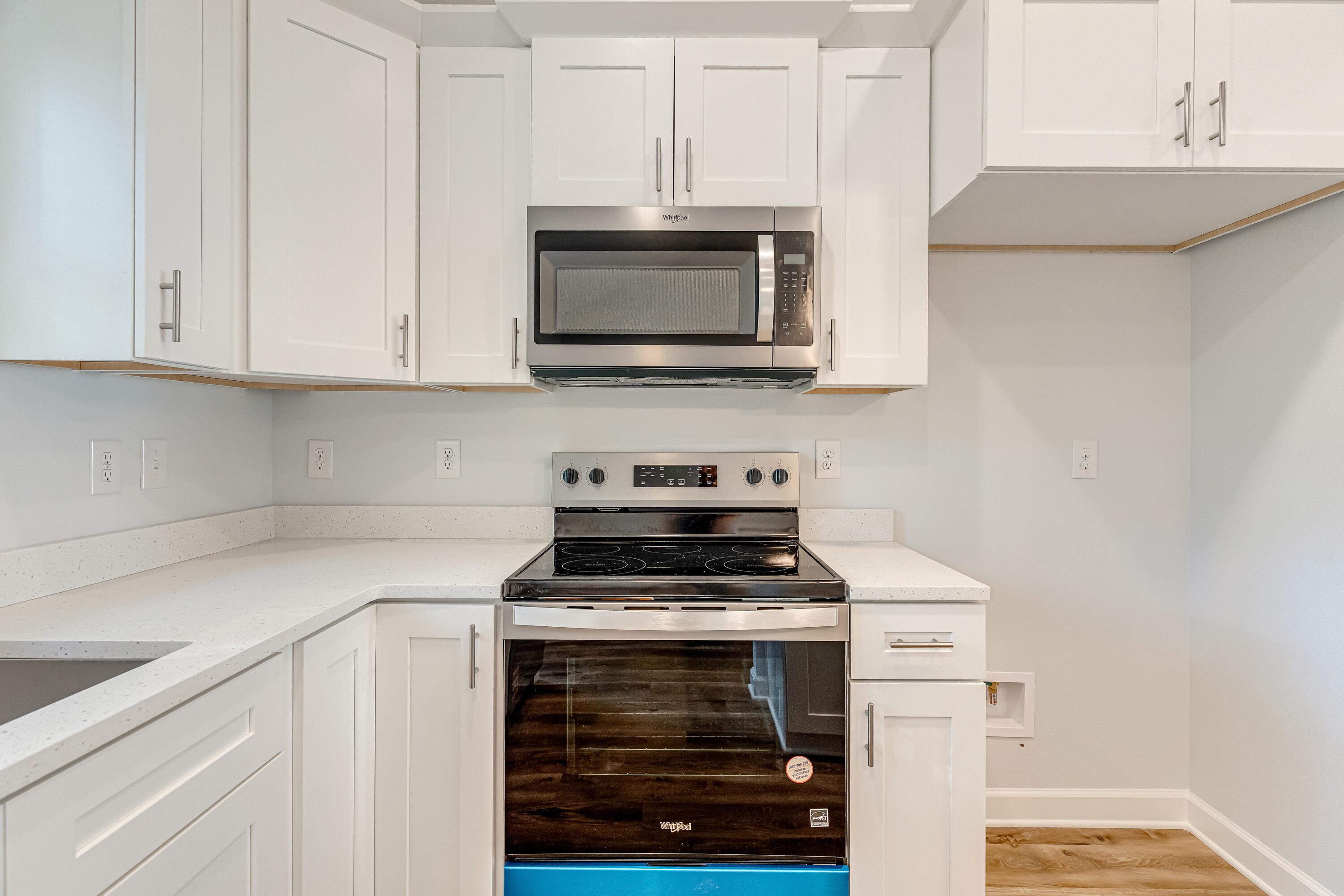 Kitchen with white cabinets, speckled counters, and a stainless steel range and microwave.