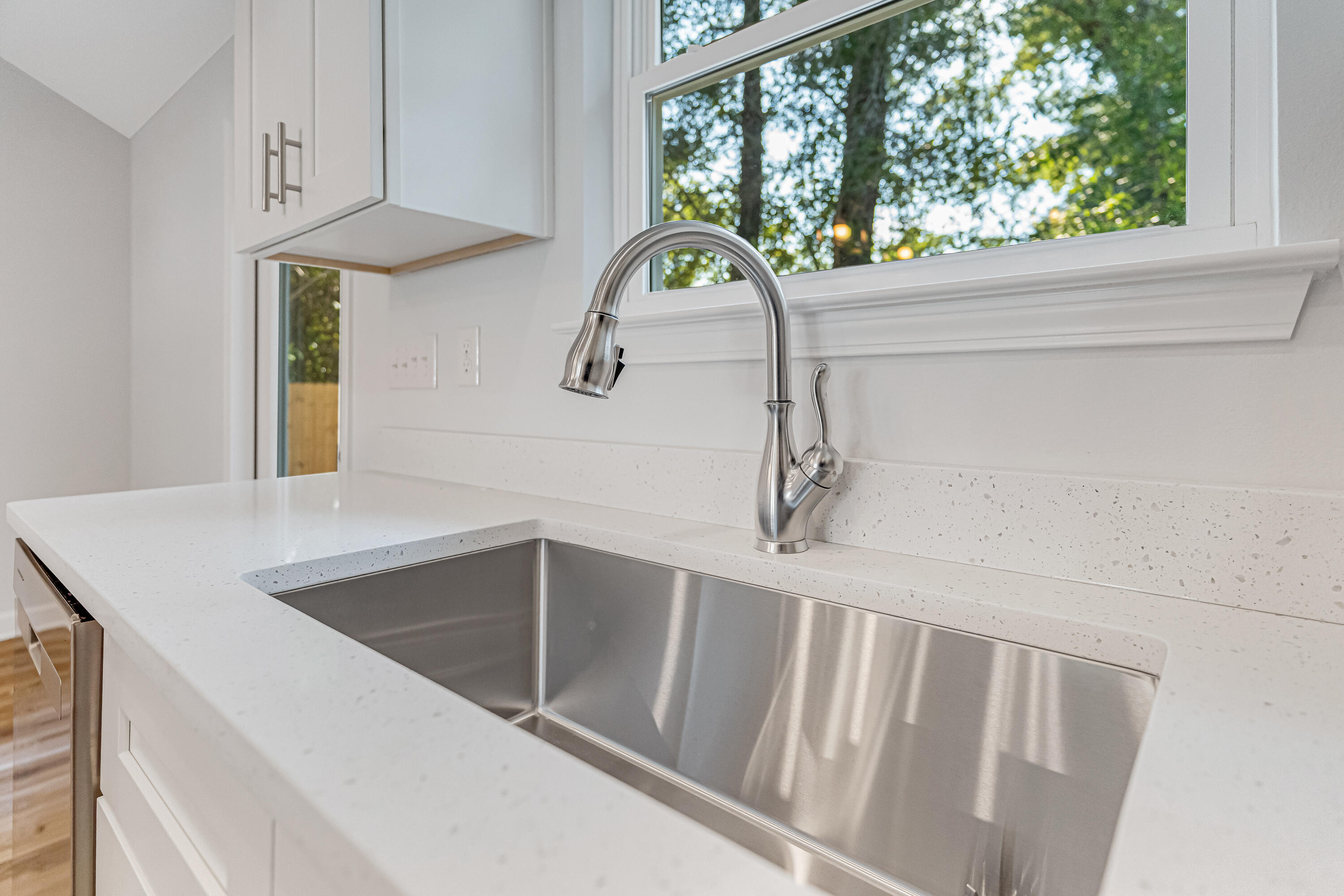 Kitchen sink with a stainless steel faucet beneath a window overlooking trees.