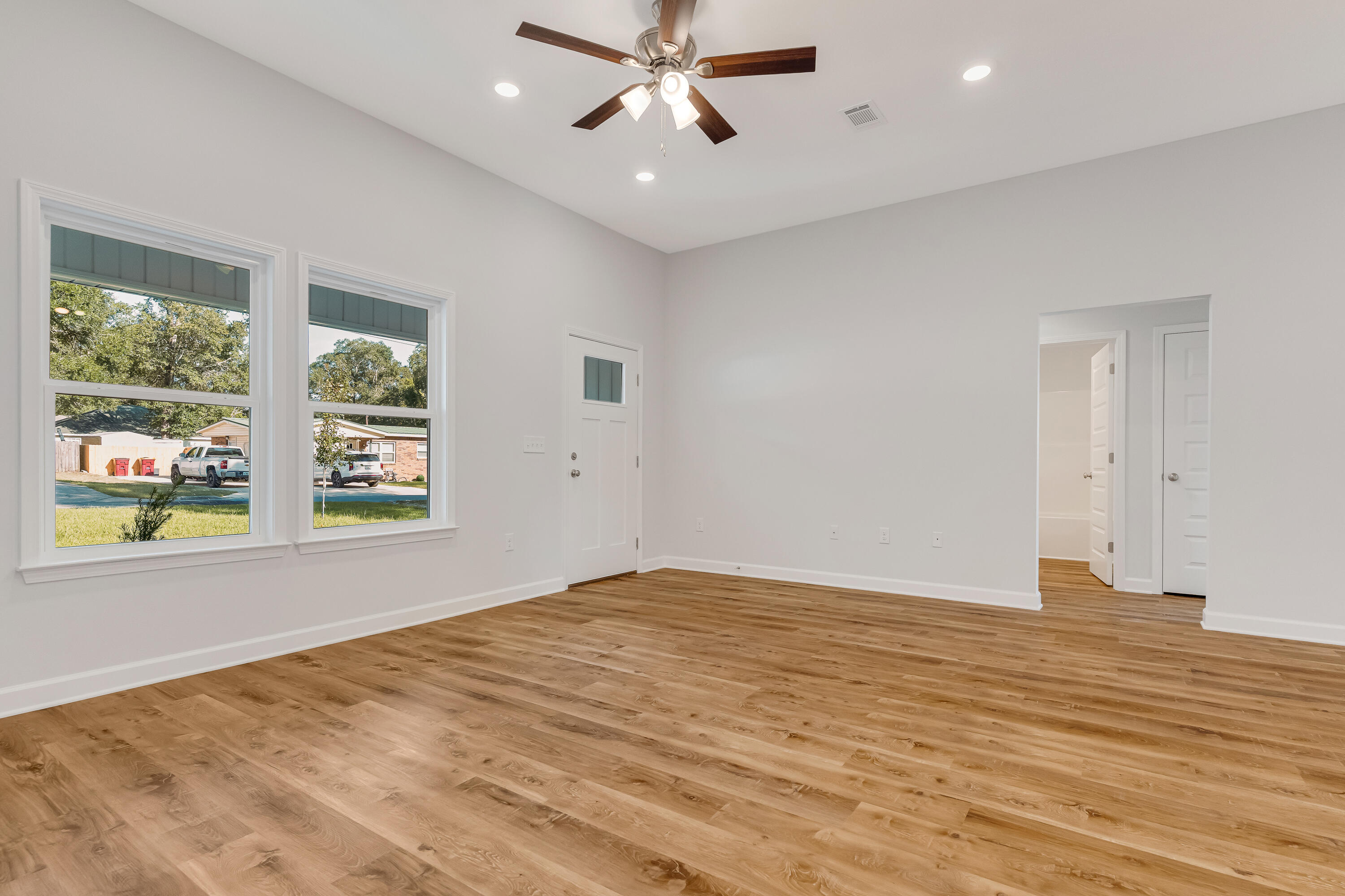 Vacant room with warm wood floors, two large windows, and a ceiling fan.