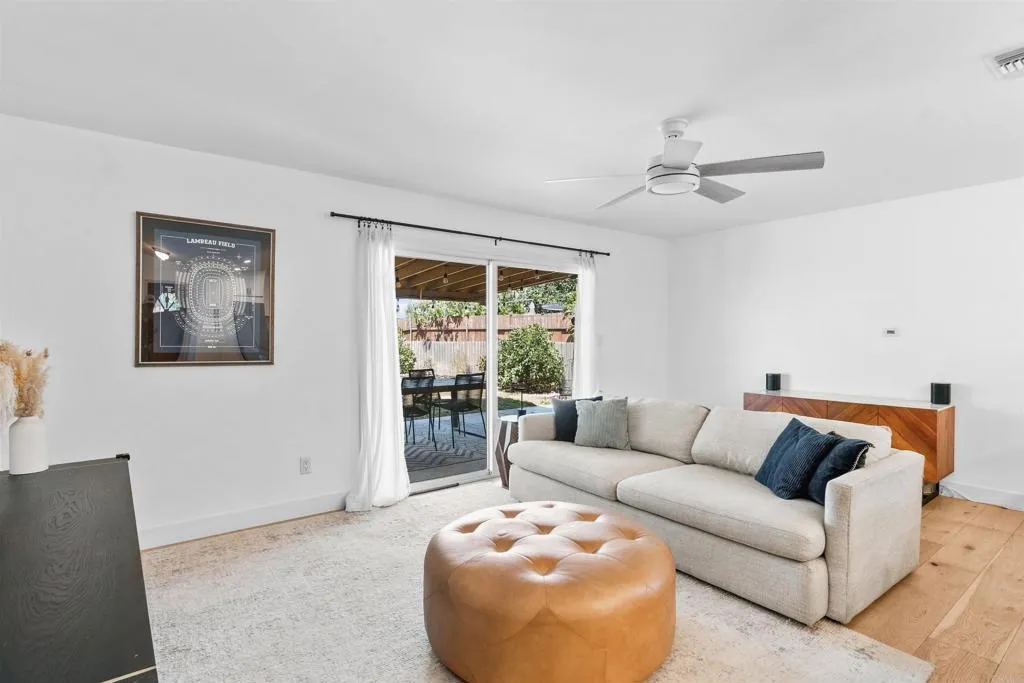 Living room with a light sectional, tan leather ottoman, and sliding doors opening to a covered patio.