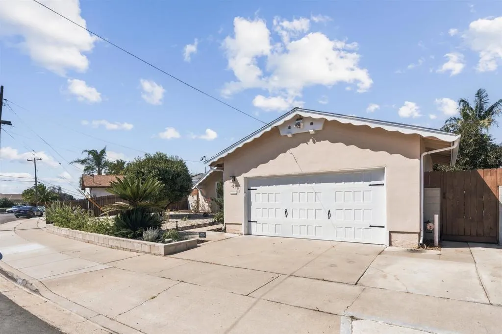 Single-story stucco home with a white double garage door, broad driveway, and landscaped front yard.