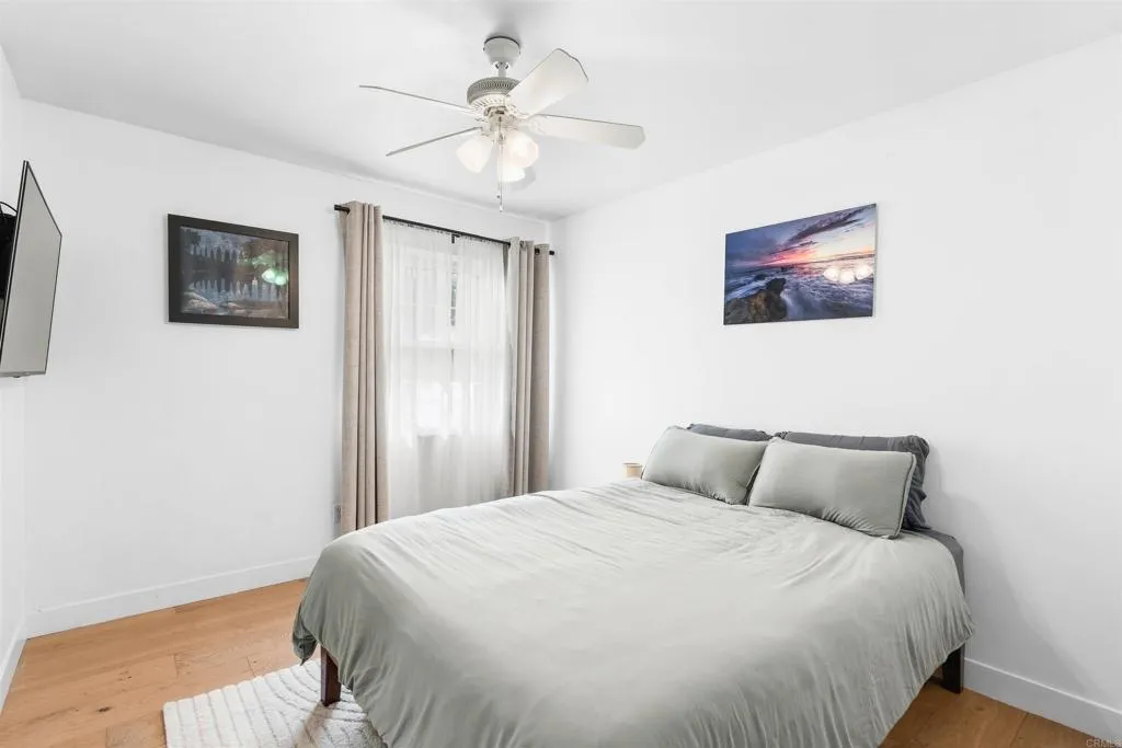 Bedroom with a large gray-bedded bed, ceiling fan, and hardwood floor.
