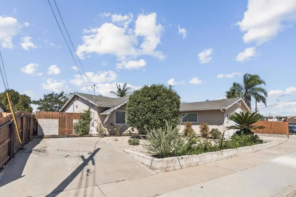 Single-story home with a wide concrete driveway, raised gravel garden bed, and wood fencing.
